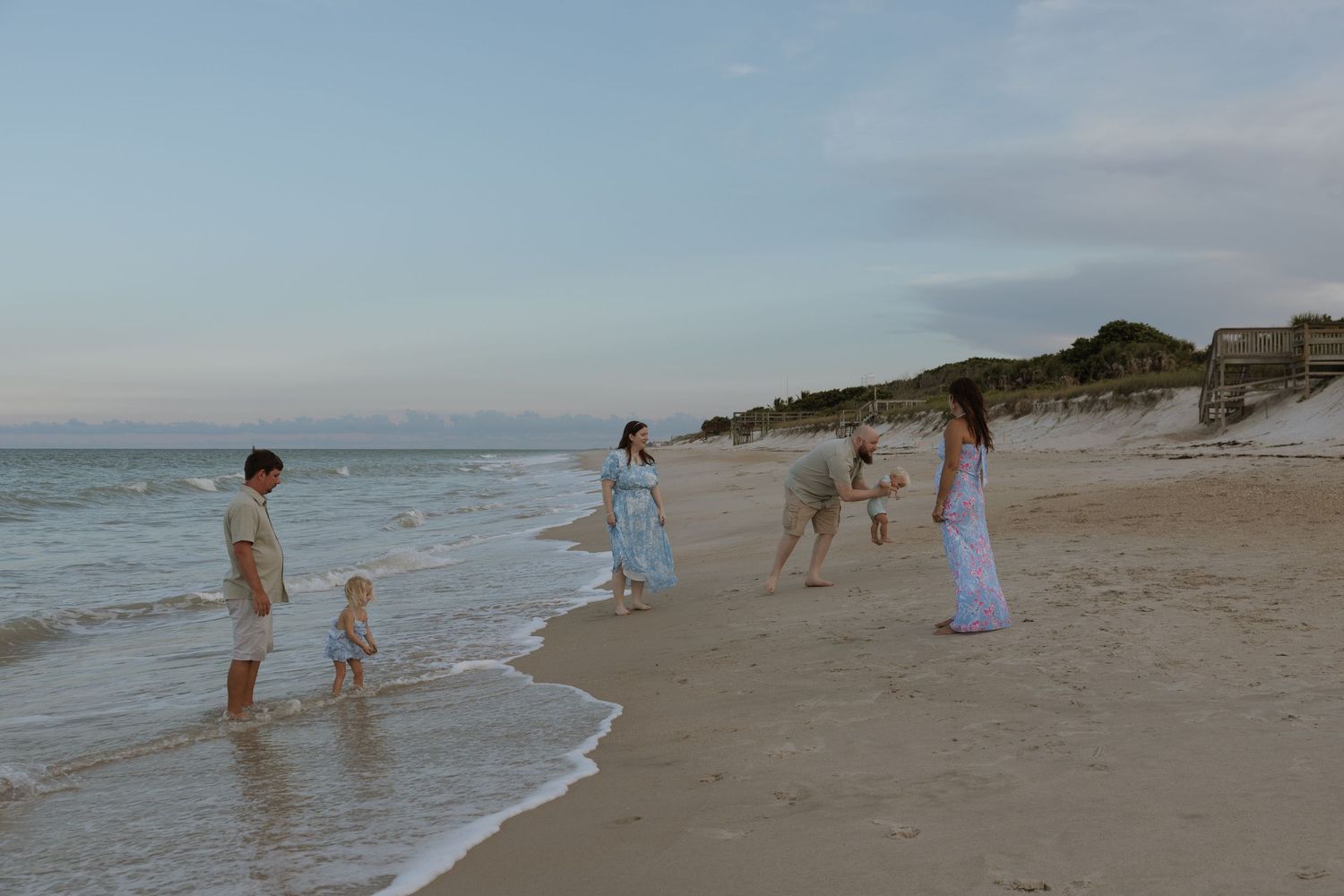 People enjoying a sunny day walking and playing along a scenic beach shoreline with waves and sand.