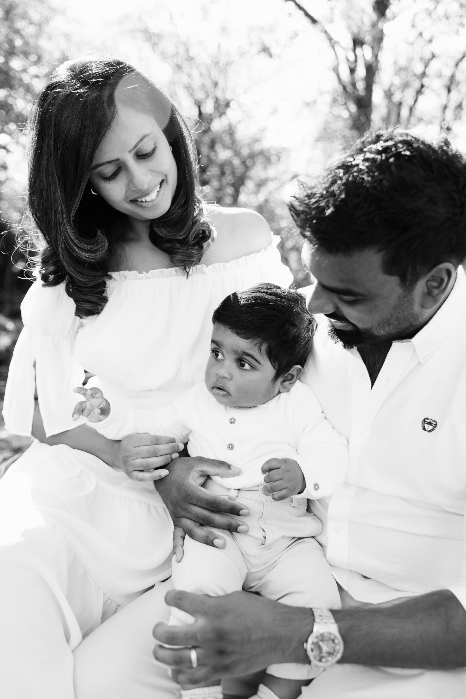 A loving family wearing white clothing shares tender moments together in black and white photos.
