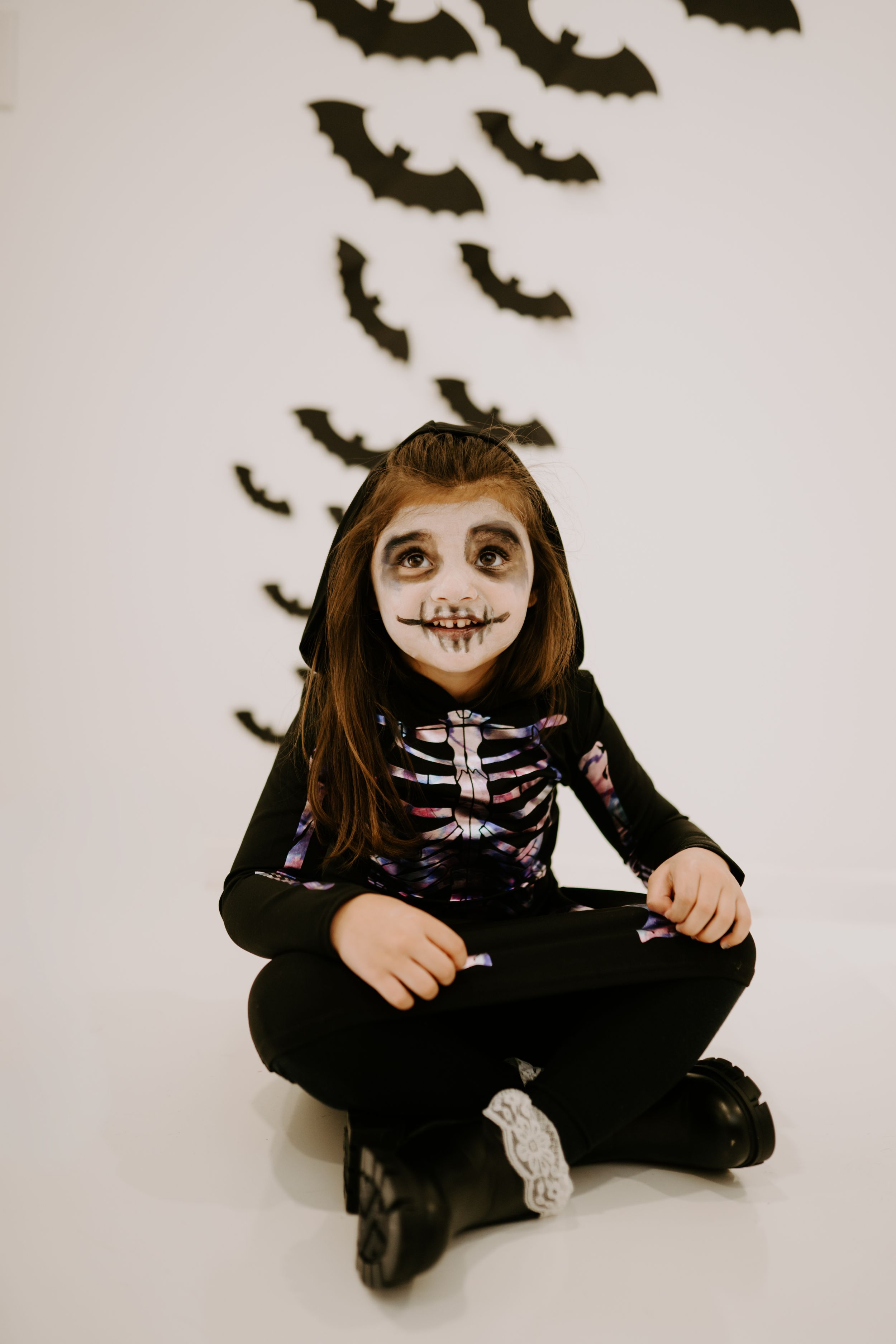 Halloween costume with skeleton makeup and black outfit against wall with bat decorations.