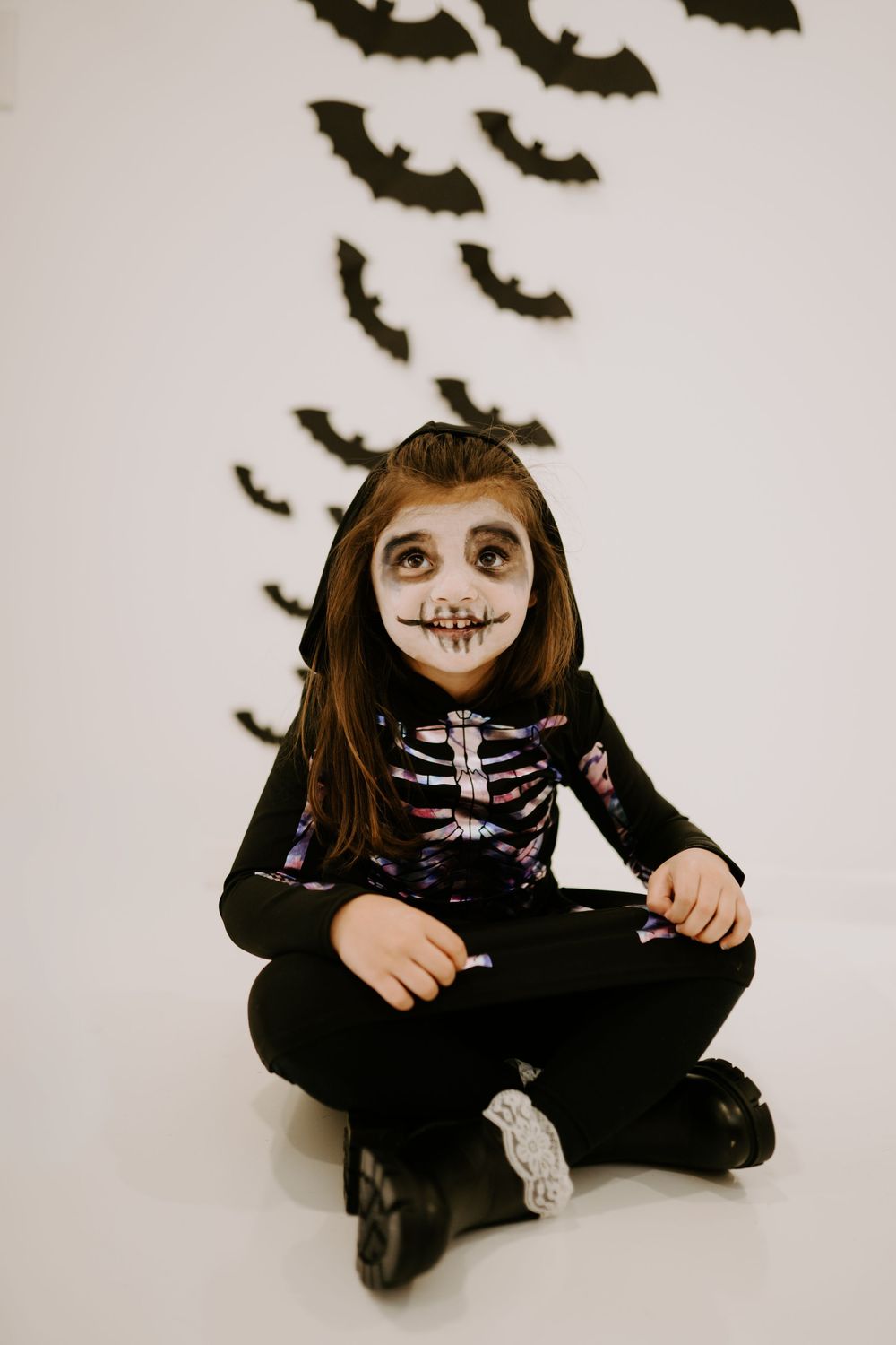 Halloween costume with skeleton makeup and black outfit against wall with bat decorations.