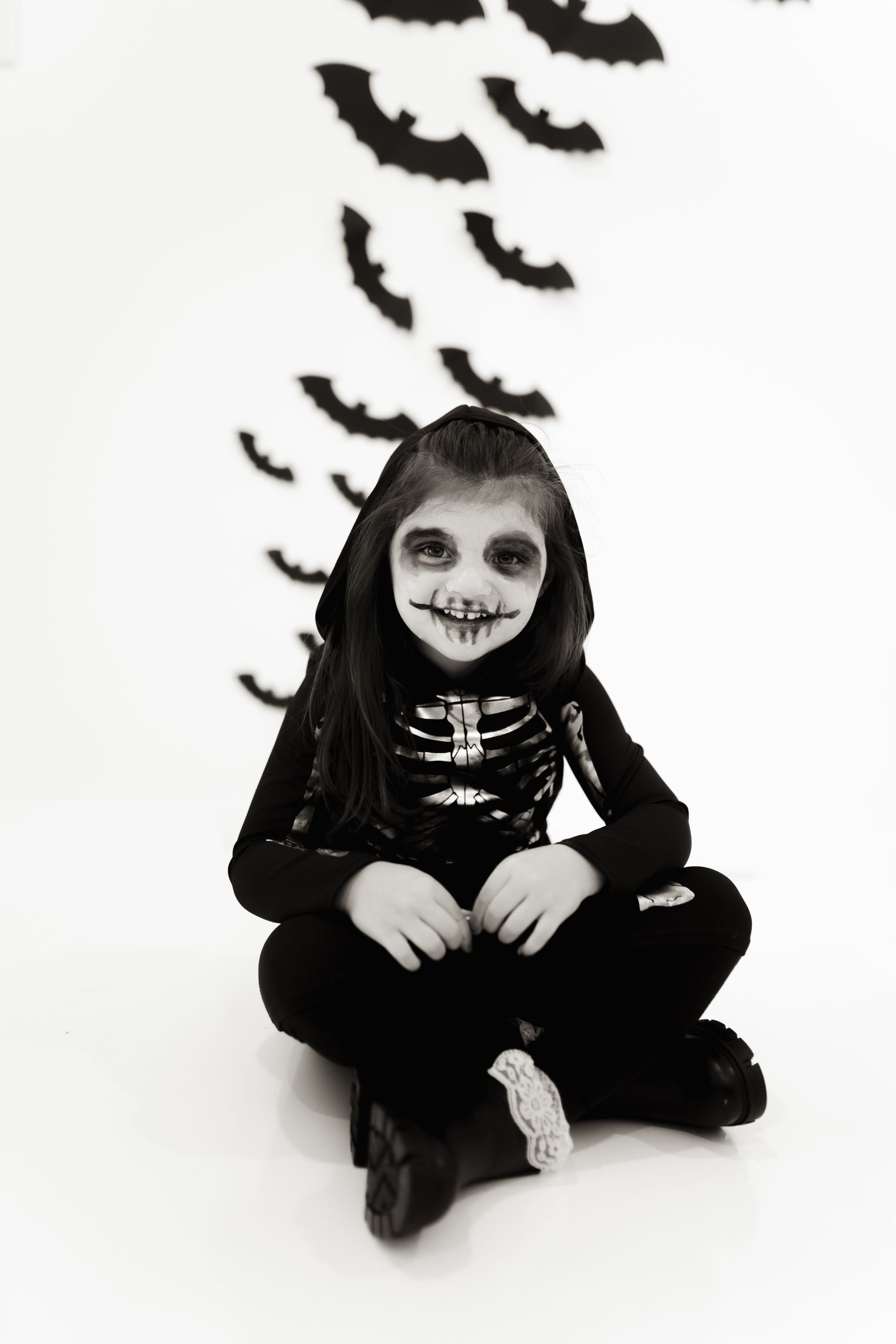 Black and white portrait of skeleton costume with flying bats in background.