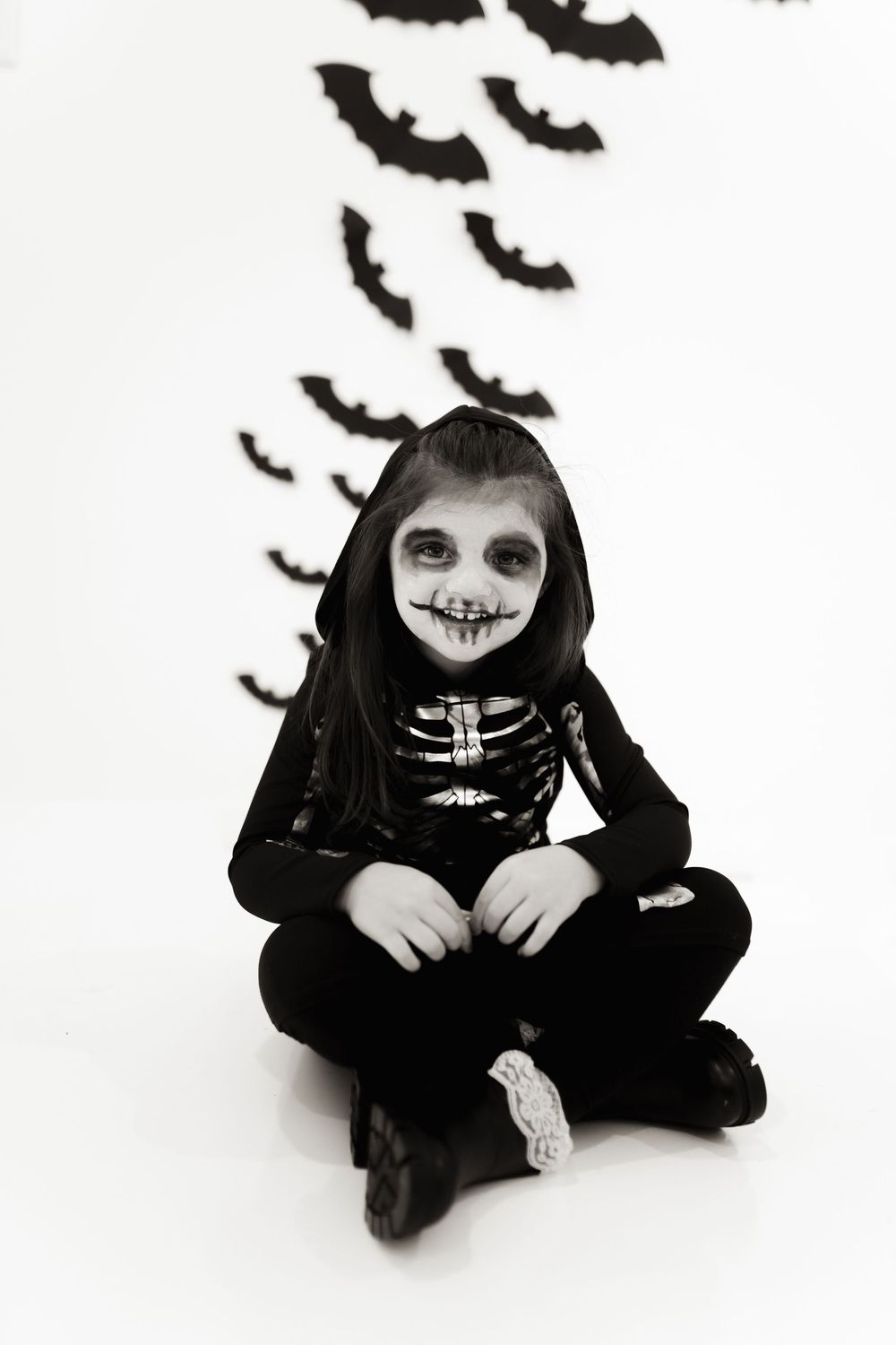 Black and white portrait of skeleton costume with flying bats in background.