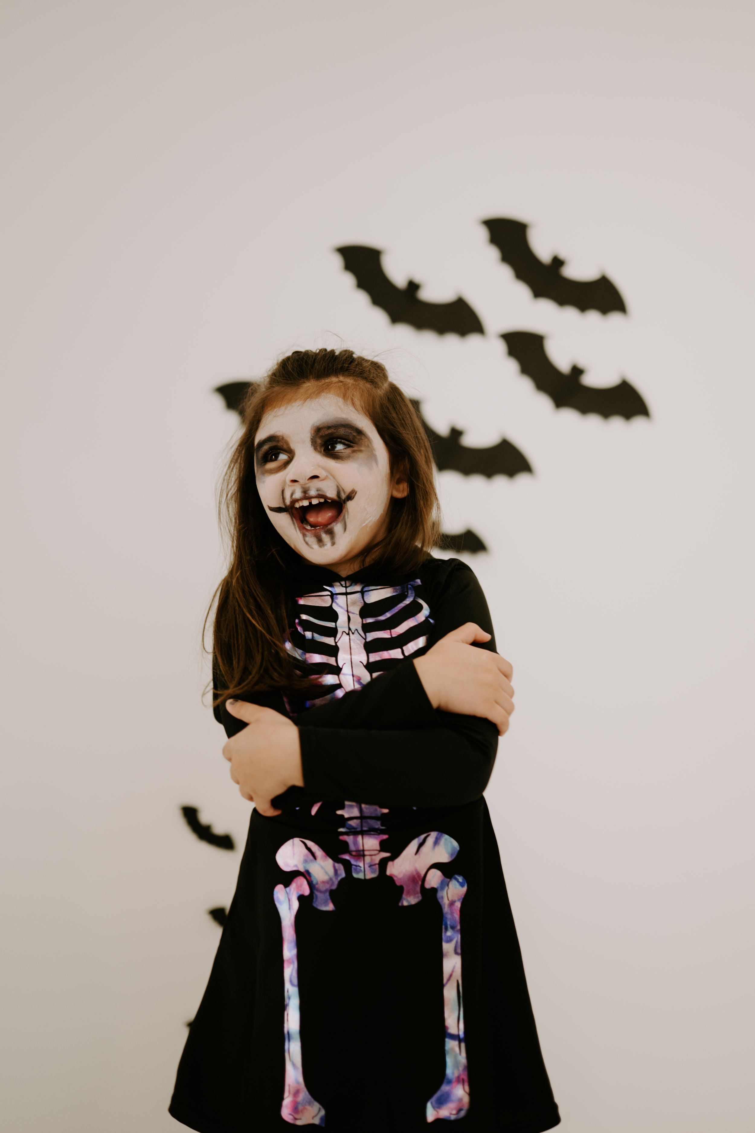 A Halloween costume featuring a black outfit with colorful skeleton design and decorative bats on the wall.