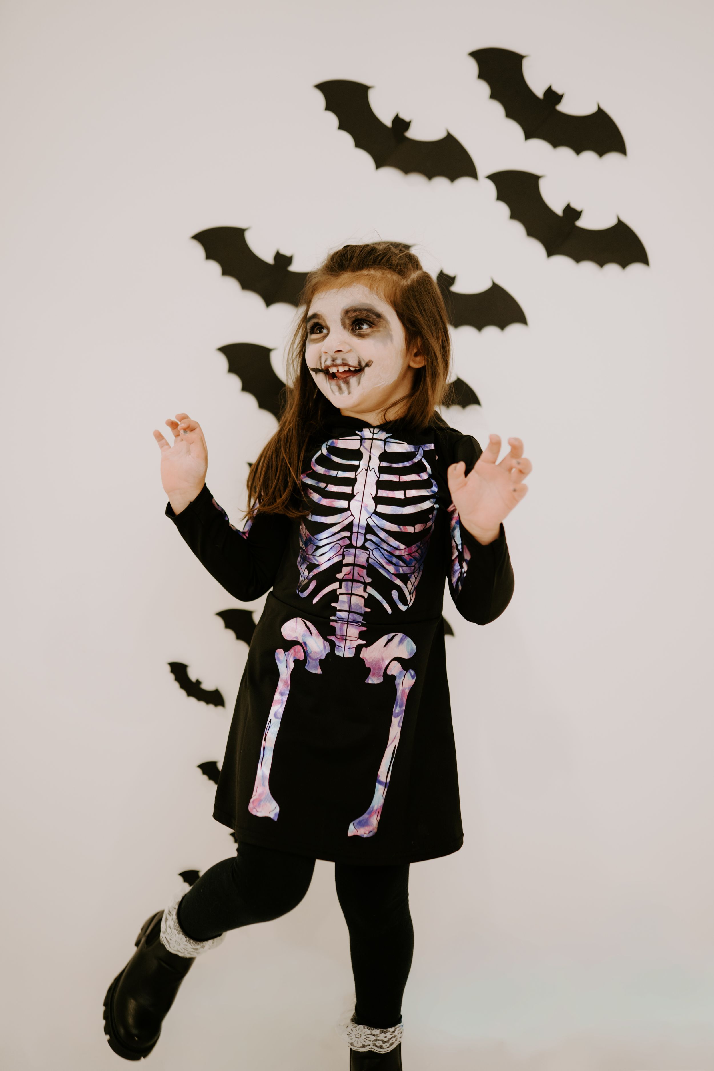 Playful Halloween pose in a skeleton costume with black wings against a white background.