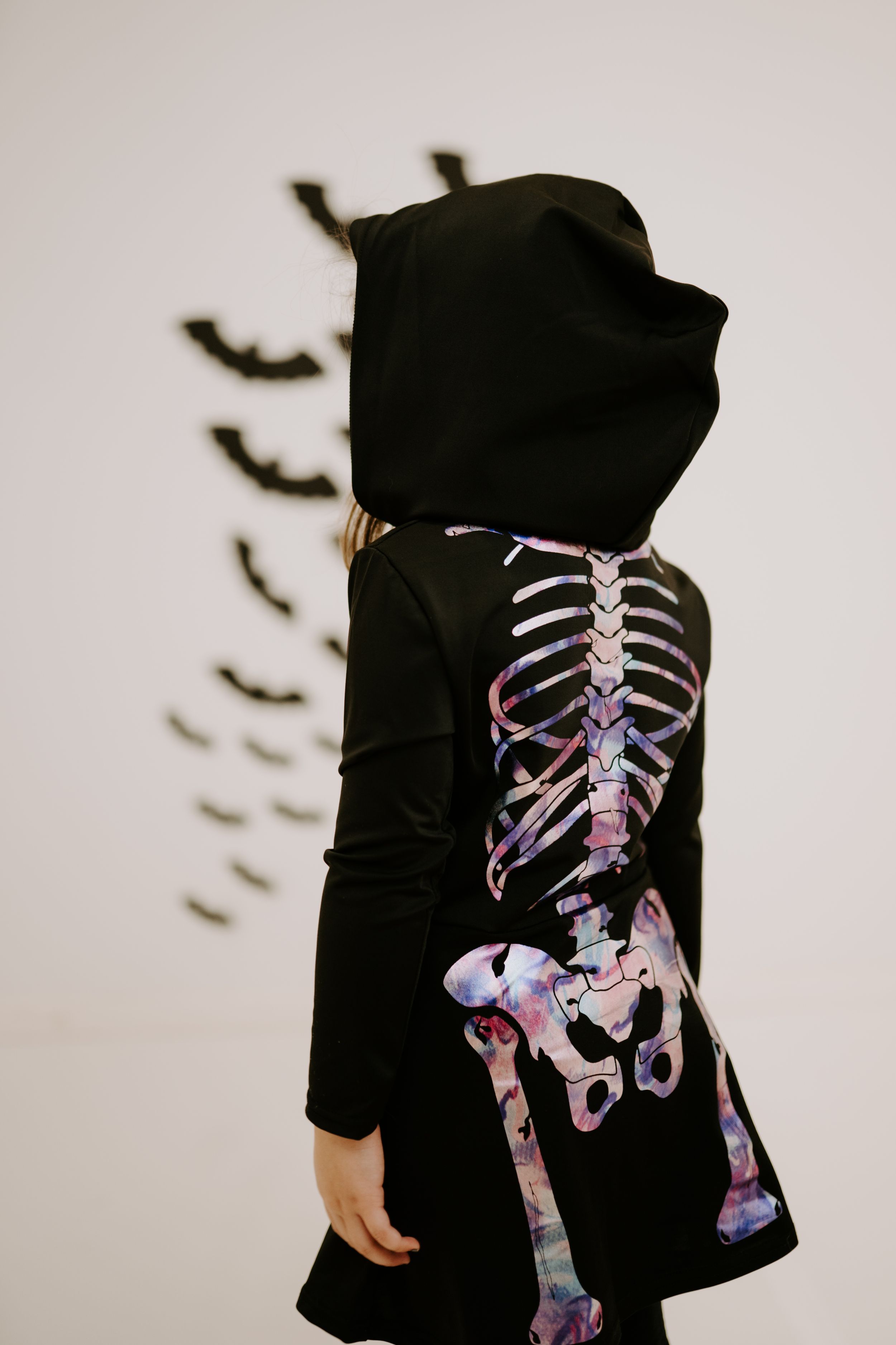 Side view of a black costume with pink and purple skeleton pattern and flying bats in background.