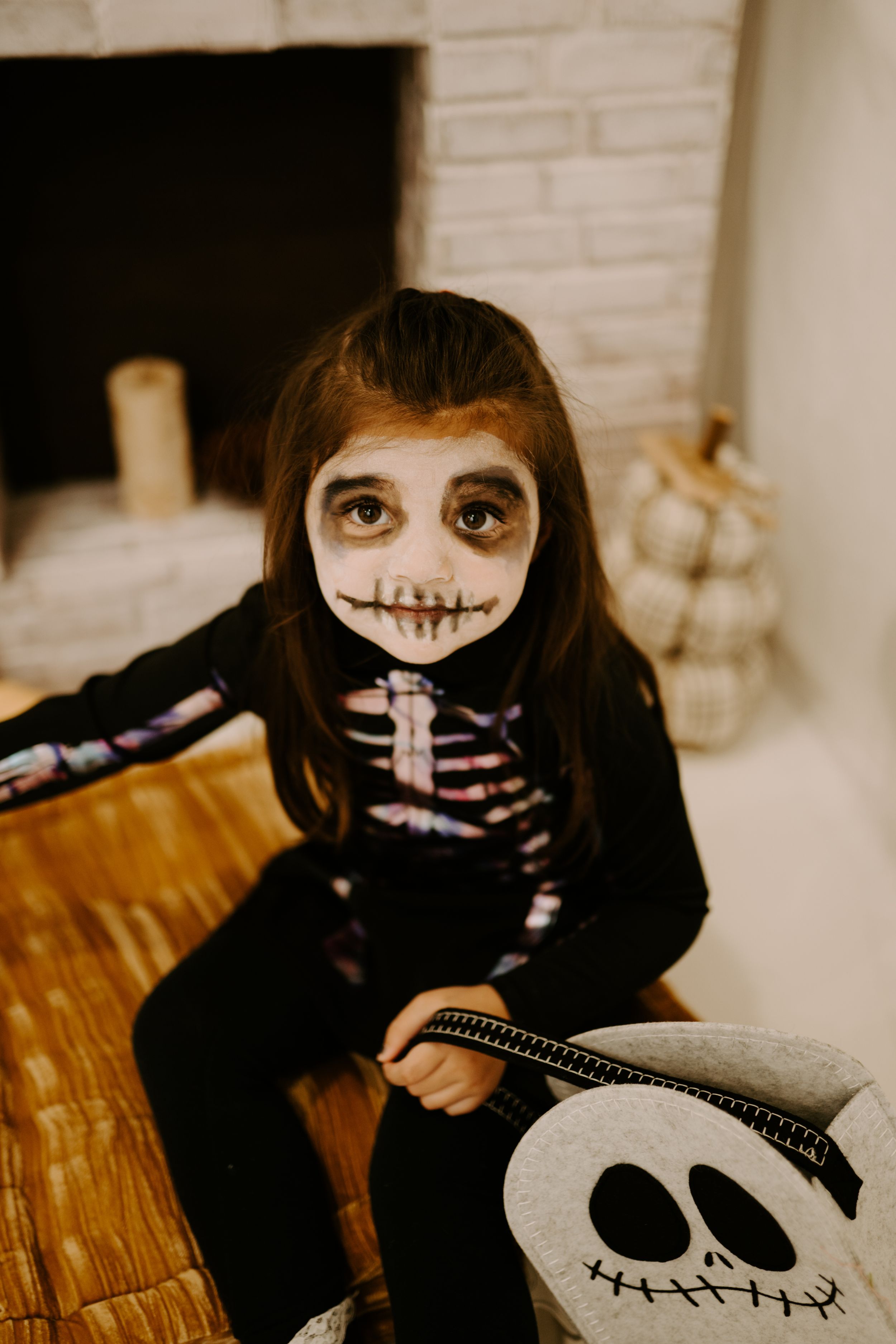 Indoor Halloween scene with skeleton costume and Jack Skellington pillow against white brick wall.