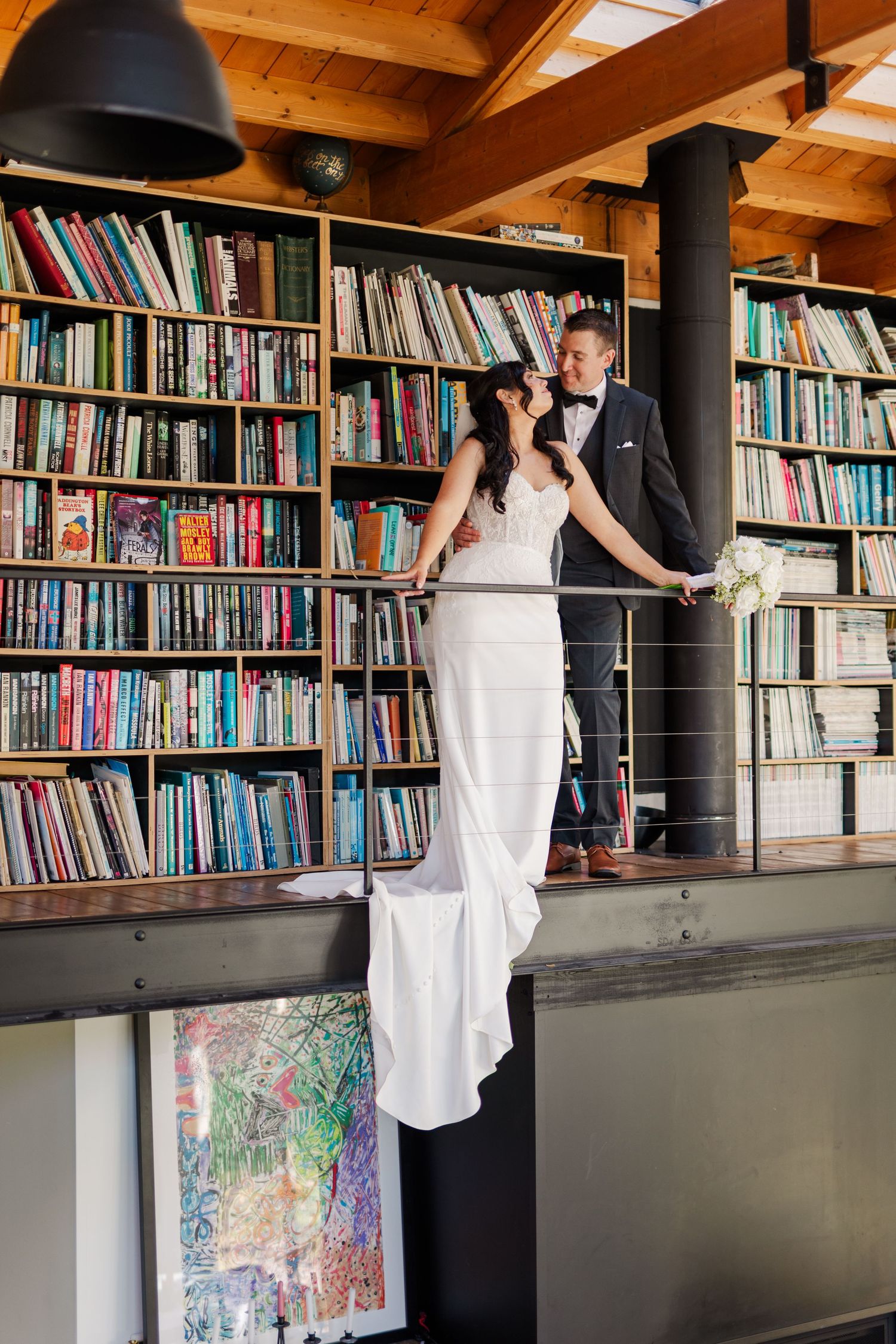 A figure in a white dress browses books in a library with wooden beams and black columns.