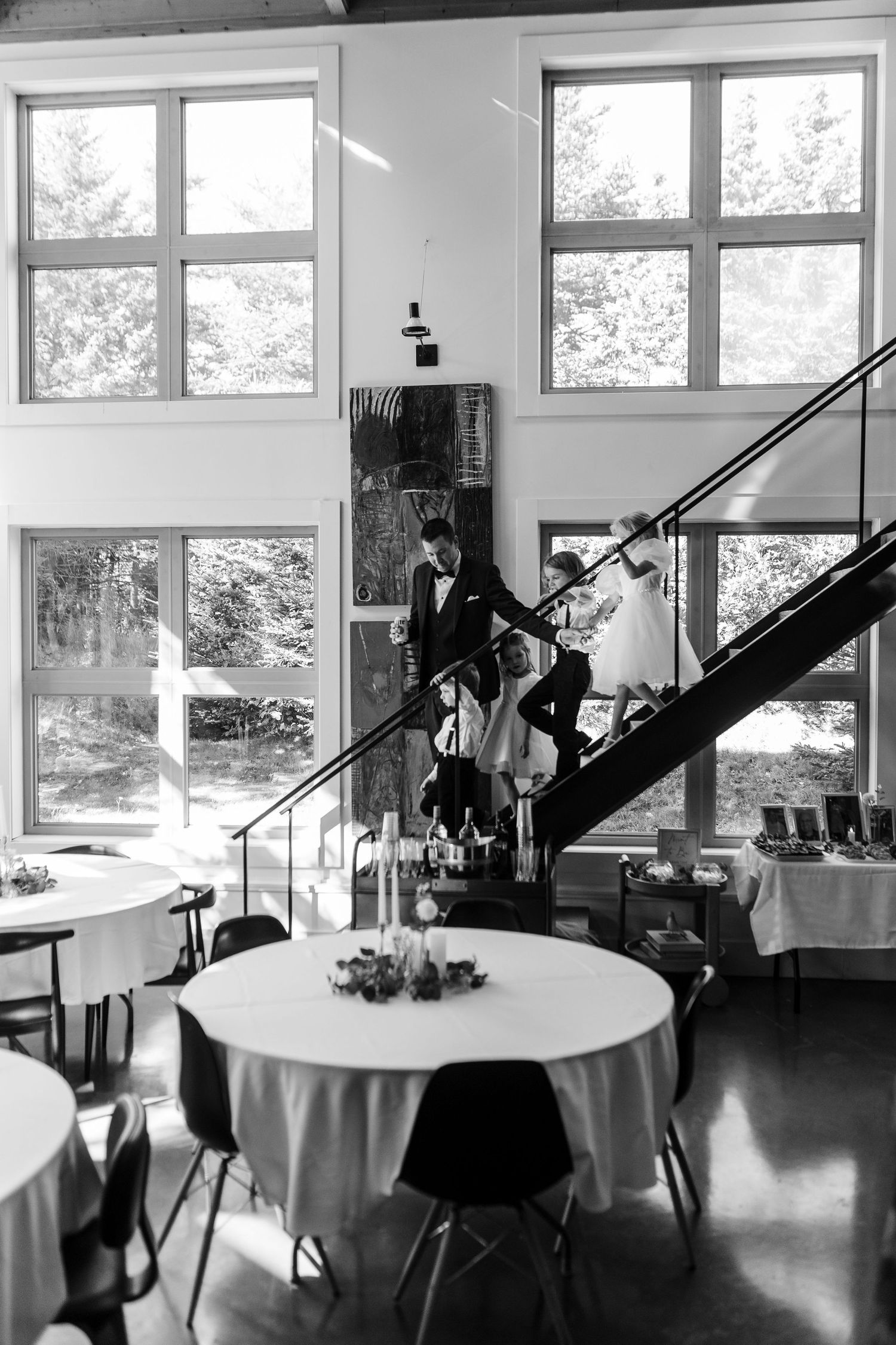 A black and white panorama of an elegant reception venue with round tables and large windows letting in natural light.