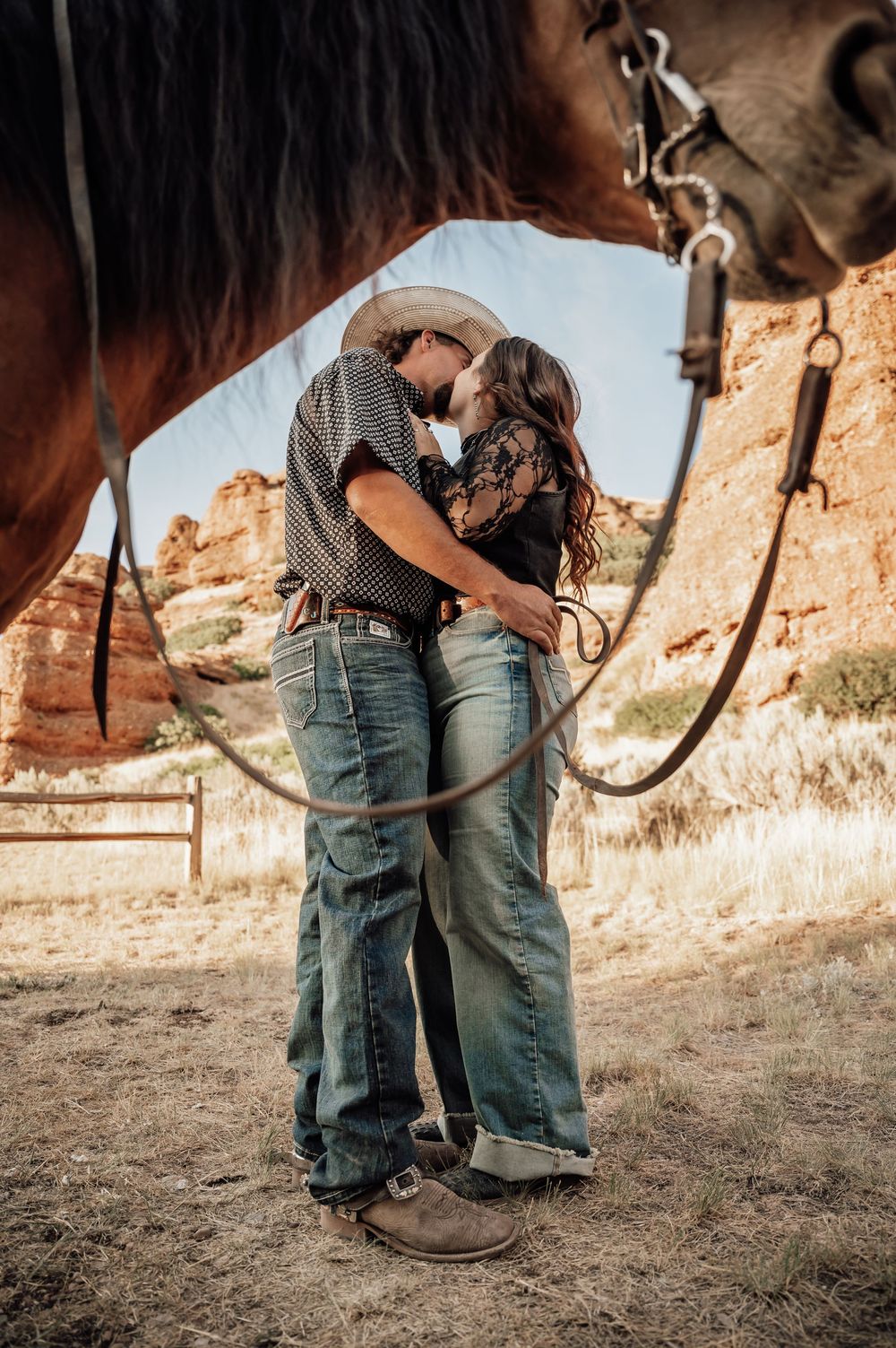 A romantic moment between two people in western attire framed by a horse's bridle and desert cliffs.