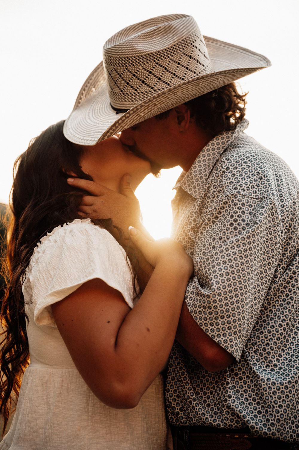 Silhouetted couple shares intimate moment at sunset wearing western attire.