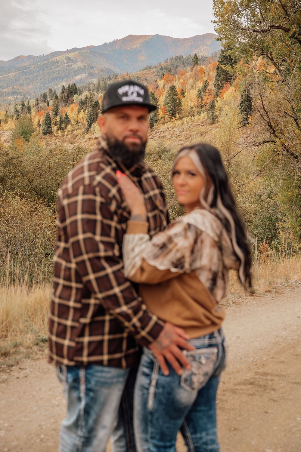 A couple in western wear embracing on a mountain trail during autumn.