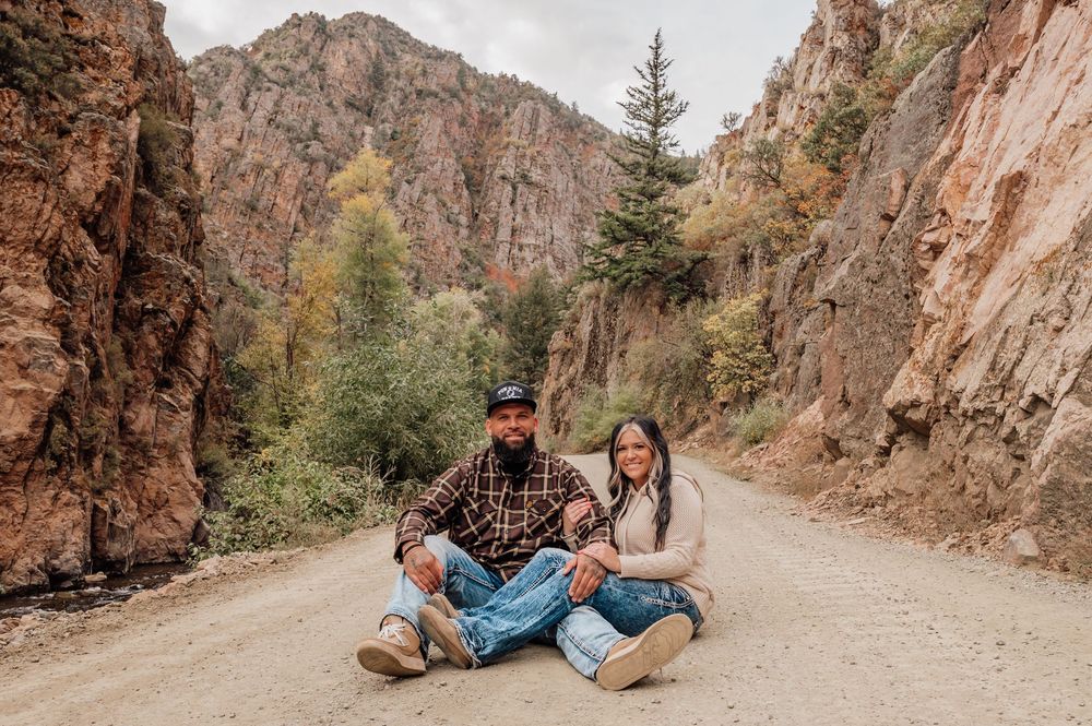 A couple sitting on a dirt road surrounded by towering red rock canyon walls.