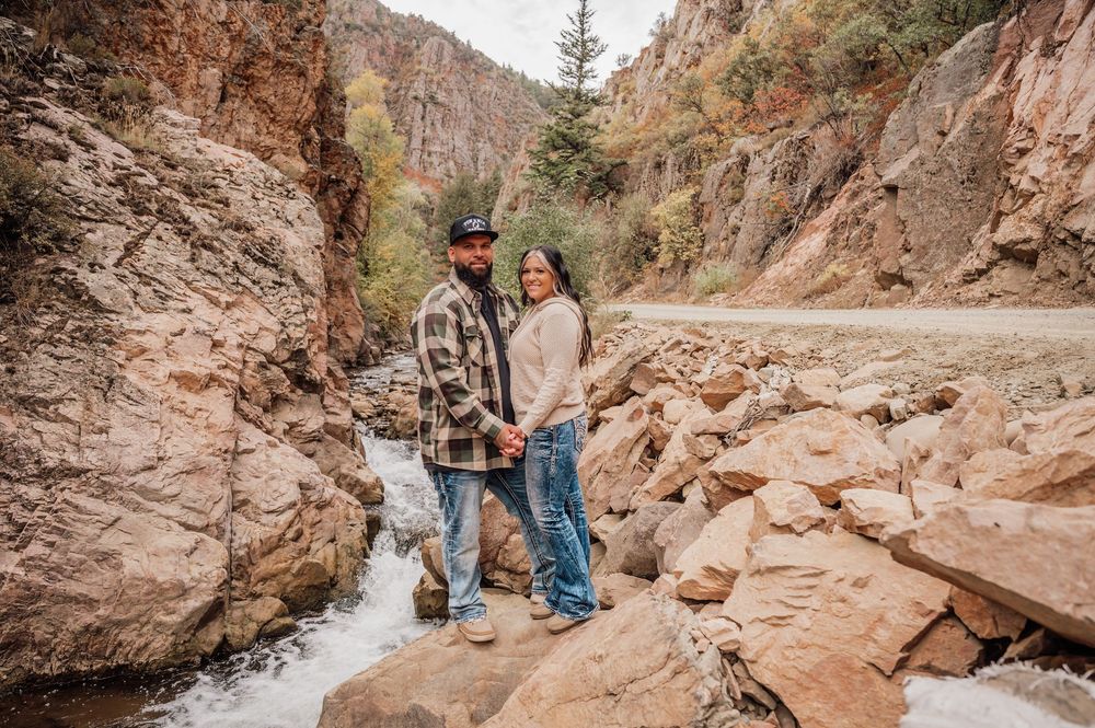 A couple exploring rocky terrain near a mountain stream in western attire.