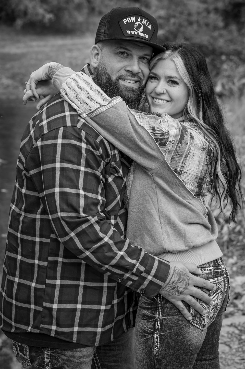 A couple in plaid and casual wear sharing an embrace in a black and white outdoor portrait.