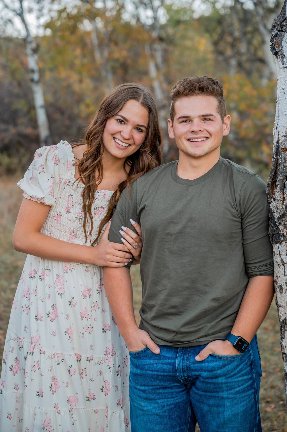 A romantic portrait of a couple in coordinated outfits standing by birch trees in fall.