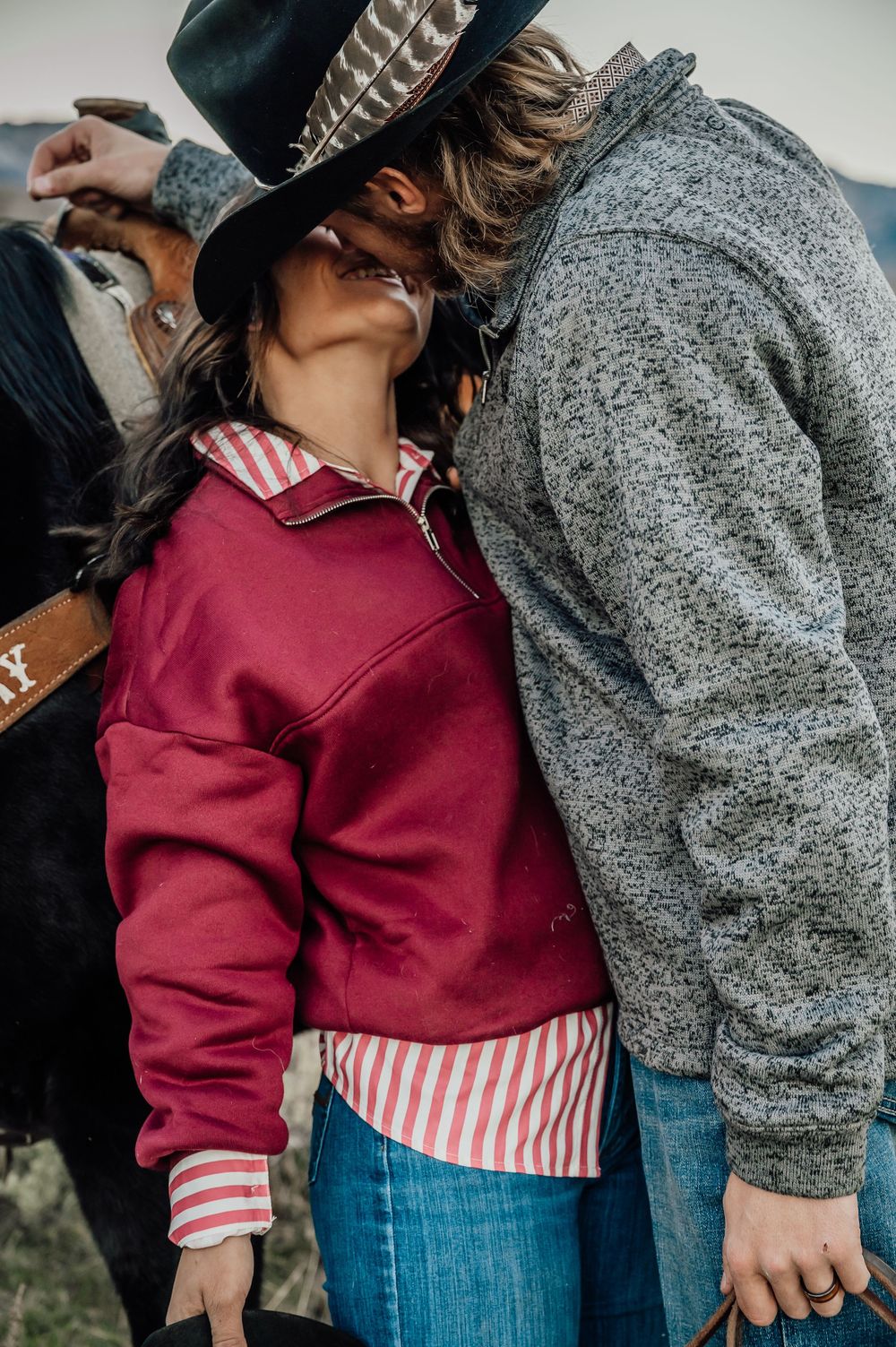 Close-up of burgundy sweater and striped shirt against gray jacket in outdoor setting.