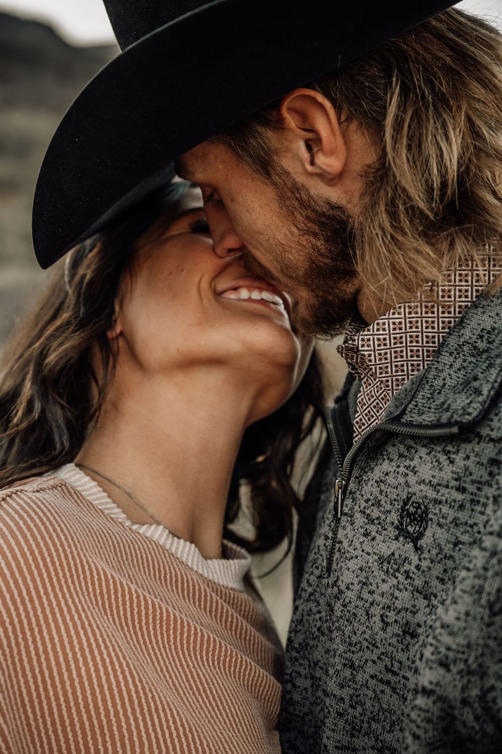 An intimate moment between a couple with one wearing a black cowboy hat against a desert backdrop.