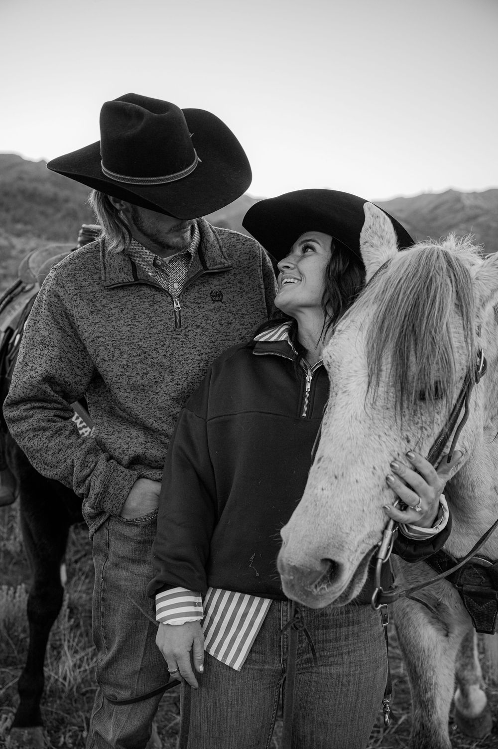 Western-themed couple's photoshoot with a white horse in black and white.