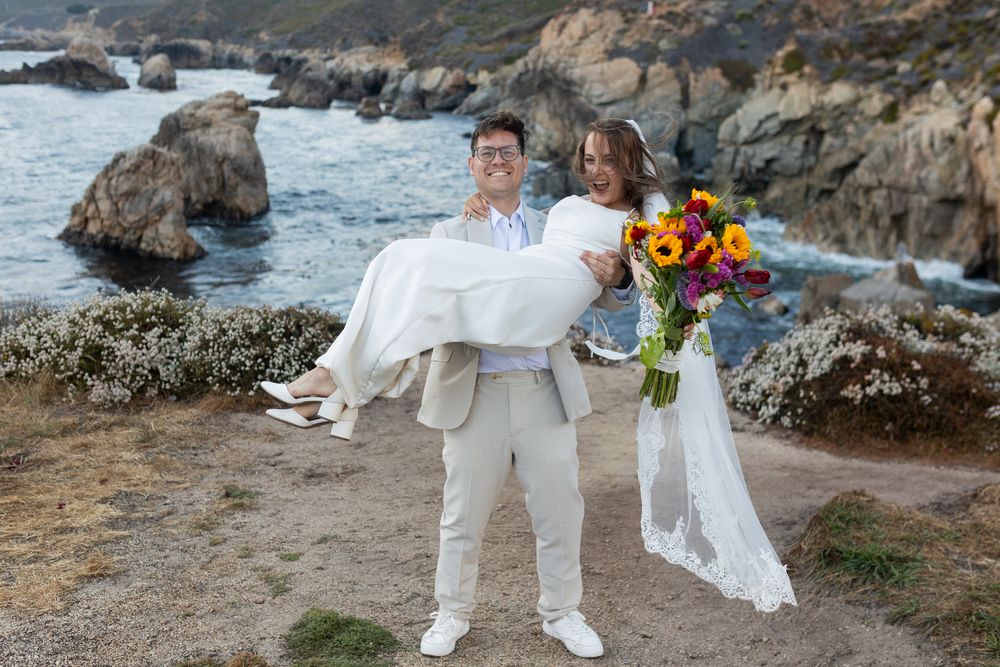 Newlyweds celebrate their wedding on a dramatic coastal overlook with colorful flowers and ocean views.