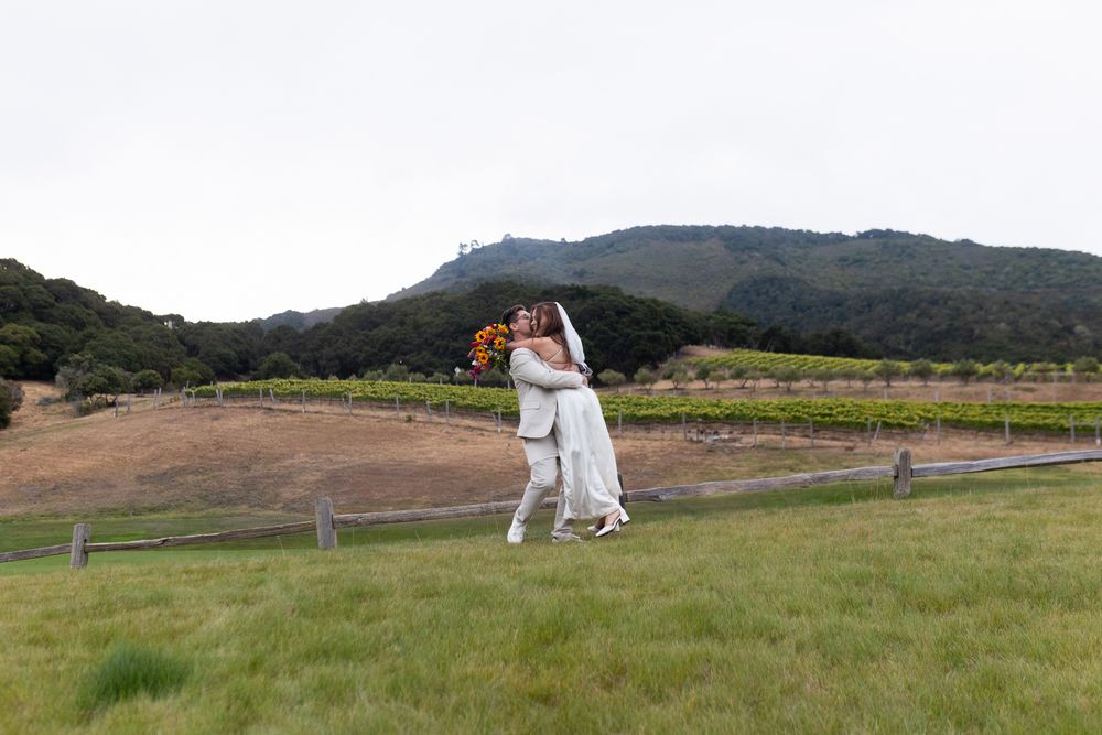 A group of people playing cricket on a grassy field with mountains in the background.