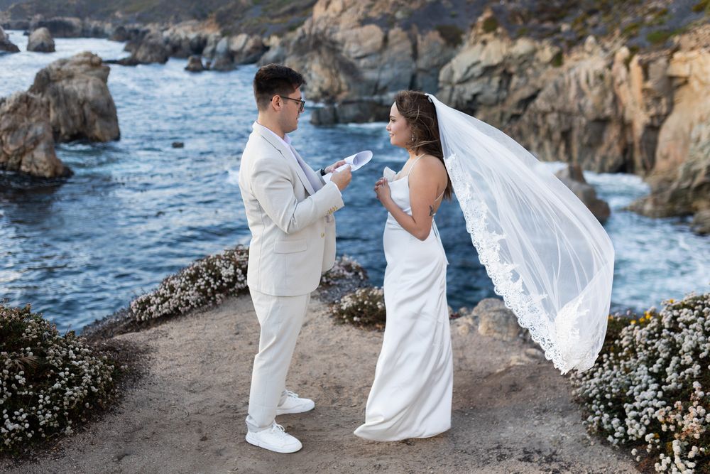 Elegant white-clad figures dance along a dramatic oceanside cliff path at sunset.