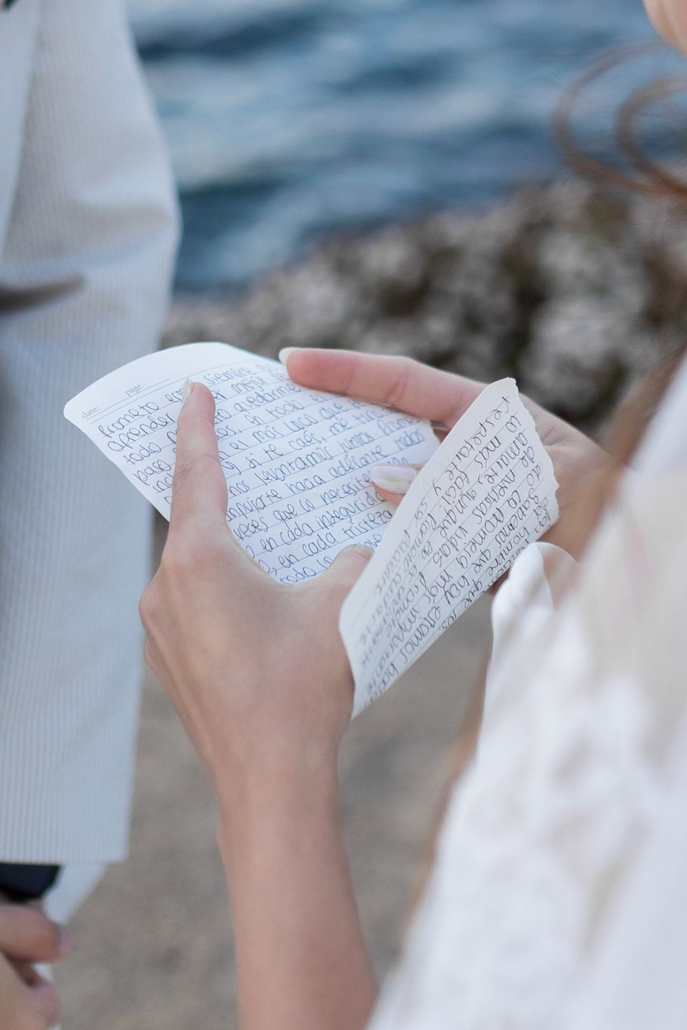 Hands holding handwritten letters or notes against a blurred water background.