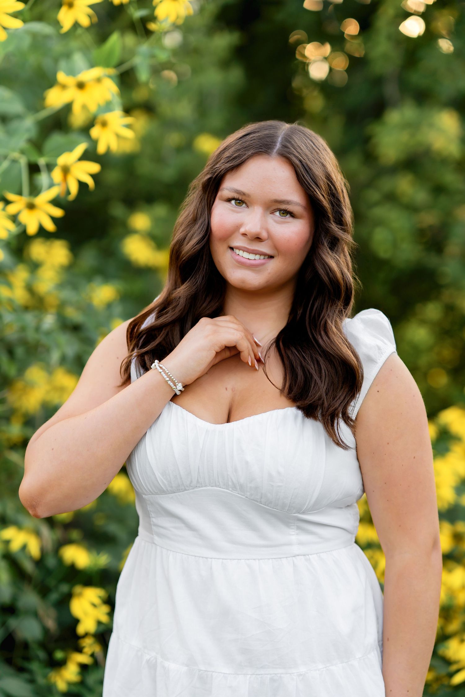 A portrait in a white summer dress against yellow flowers and greenery in soft natural lighting.