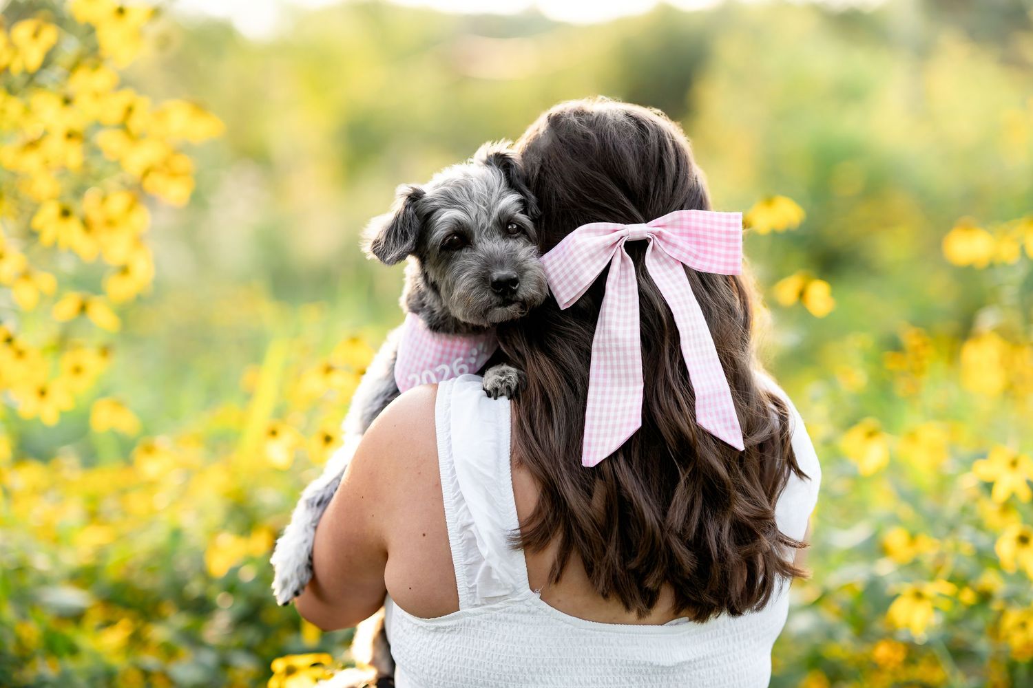 Children with bows in their hair pose together in a field of bright yellow wildflowers on a sunny day.