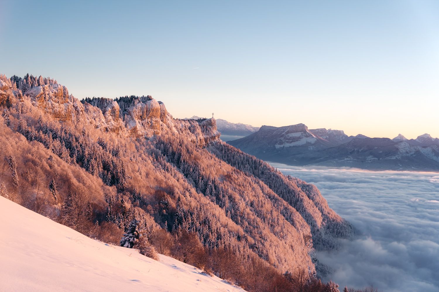 Coucher de soleil sur la croix du Nivolet en hiver avec de la neige et une mer de nuages