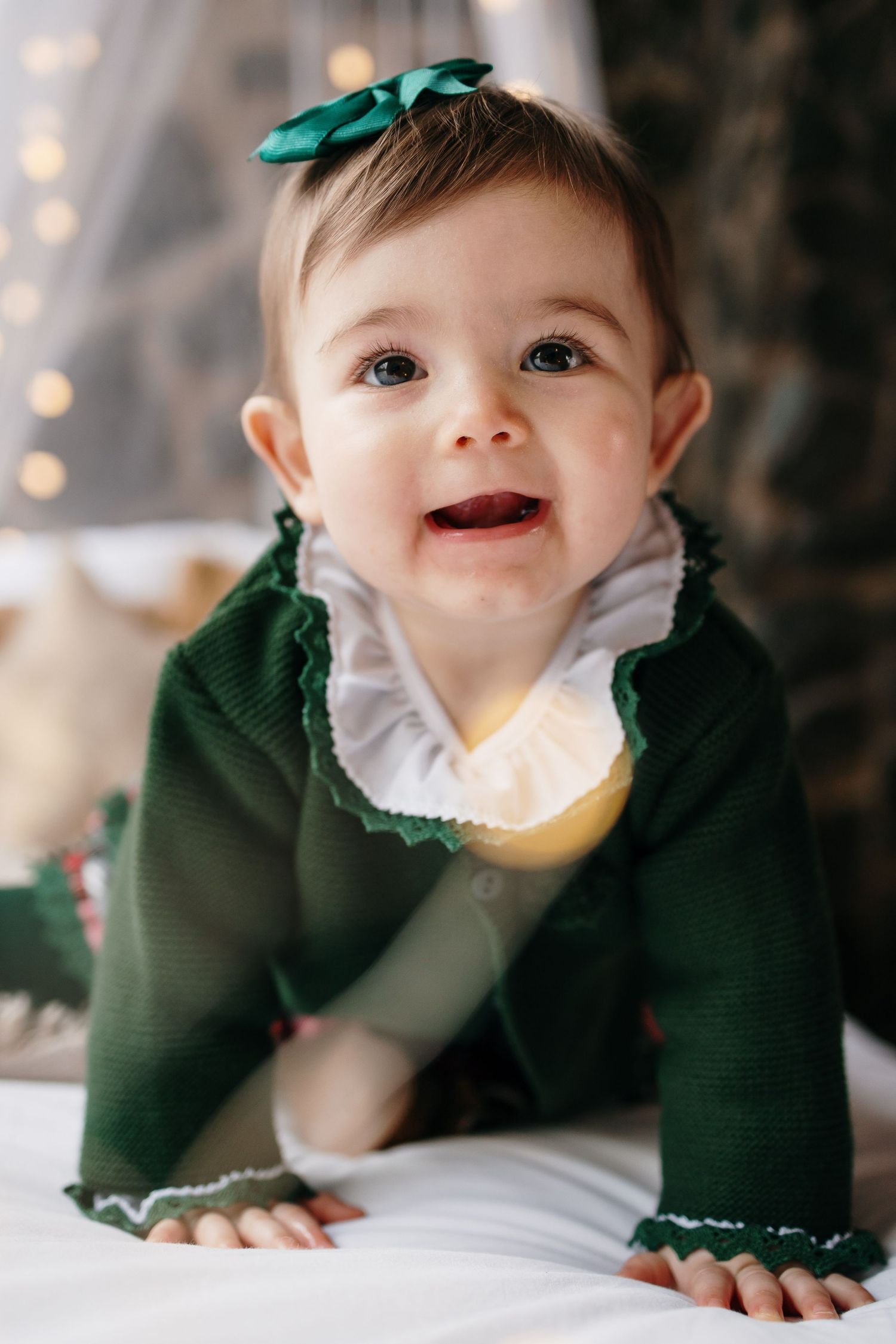 Baby in green holiday outfit smiles during Christmas portrait session.
