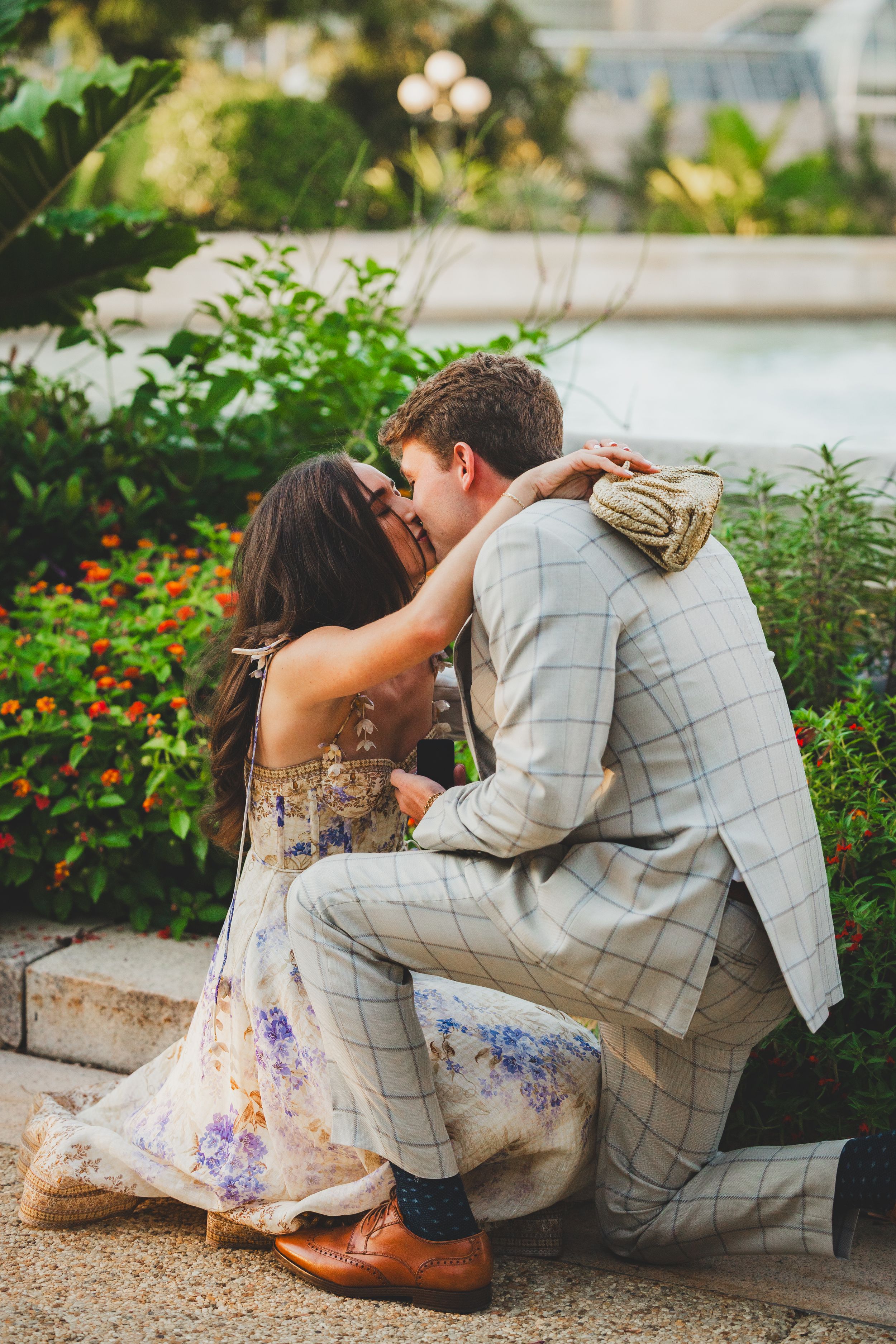 A romantic proposal moment captured in a garden setting with blooming flowers and greenery.
