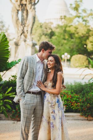 A couple shares joyful laughter together in a garden setting wearing a gray plaid suit and floral dress.