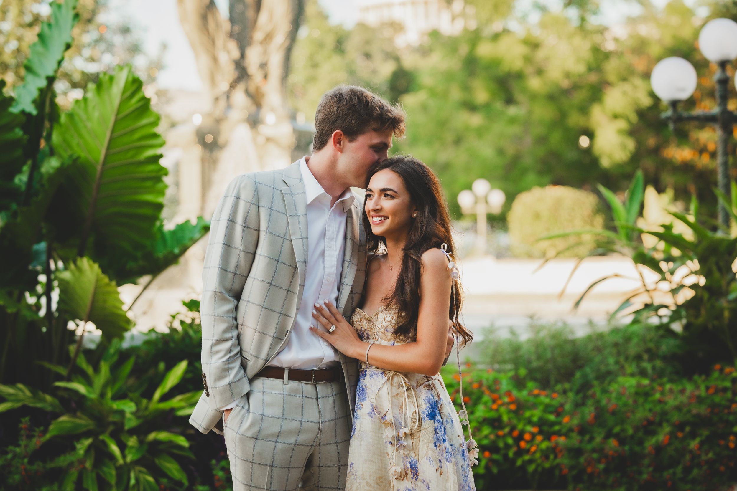 A couple shares romantic moments together in a lush garden setting with blooming flowers and greenery.