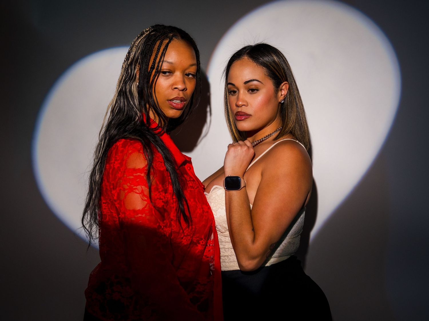 Two models pose dramatically in contrasting red and black outfits against a dark background with dramatic lighting.