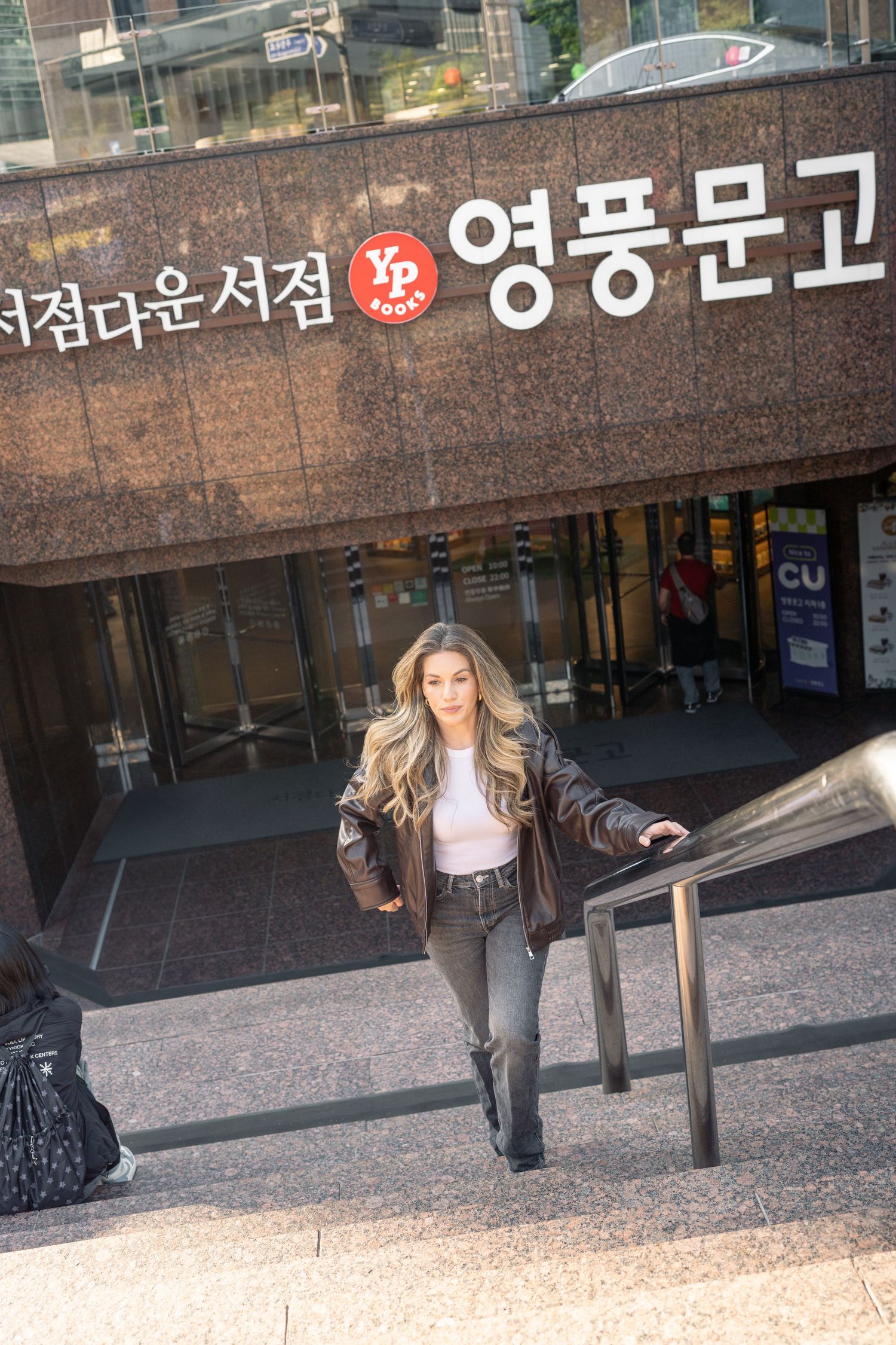 A person stands in front of a Korean storefront with signage visible in the background.