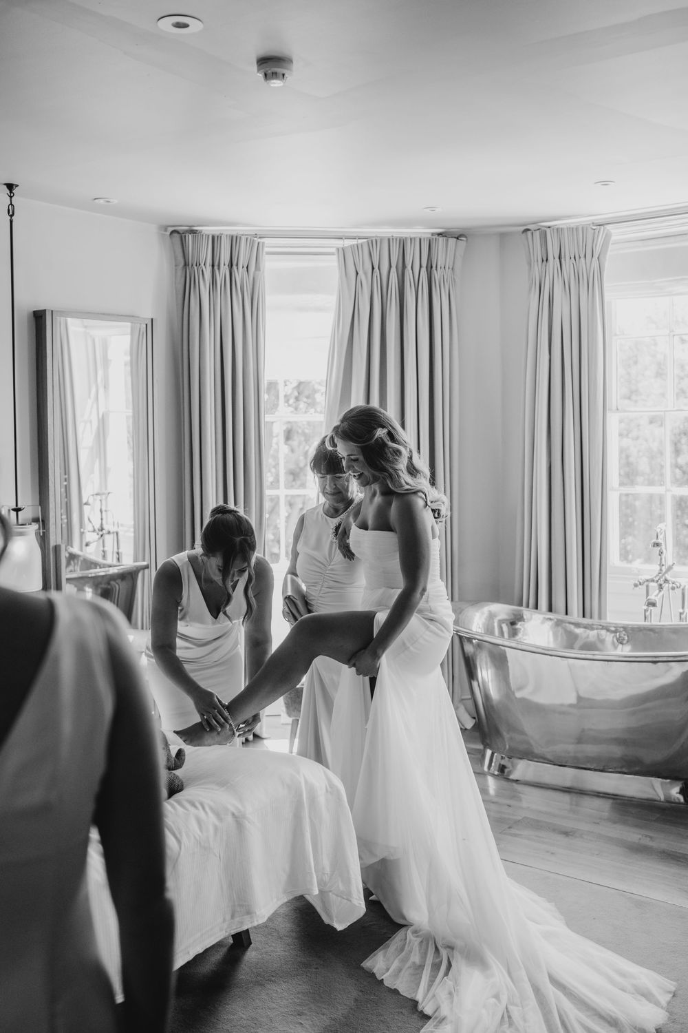 Black and white photo series showing the process of putting on a wedding dress in an elegant room with flowing curtains.