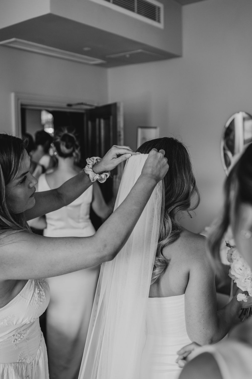 A sequence of black and white photos showing a bride getting ready with bridesmaids helping with her veil.