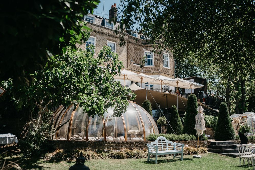 A rustic outdoor wedding venue with string lights and wooden benches surrounded by lush green trees and foliage.