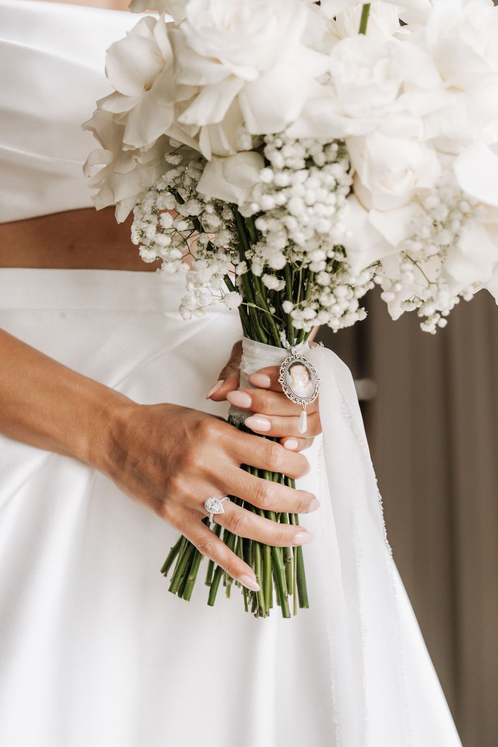 Close-up view of hands holding an elegant white floral bouquet with baby's breath against a white wedding dress.