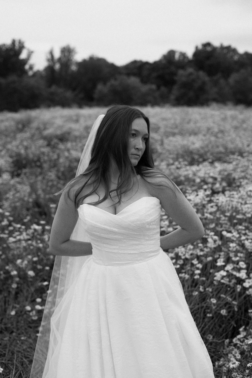 A figure in a flowing white dress poses gracefully in a field of wildflowers on a summer day.