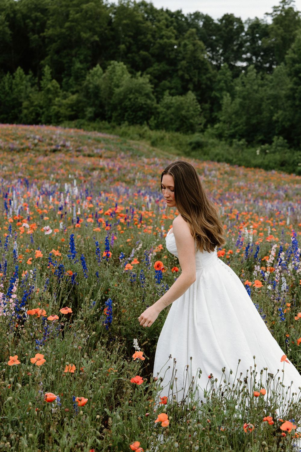 A white dress flows through a vibrant meadow filled with orange poppies and purple wildflowers on a summer day.