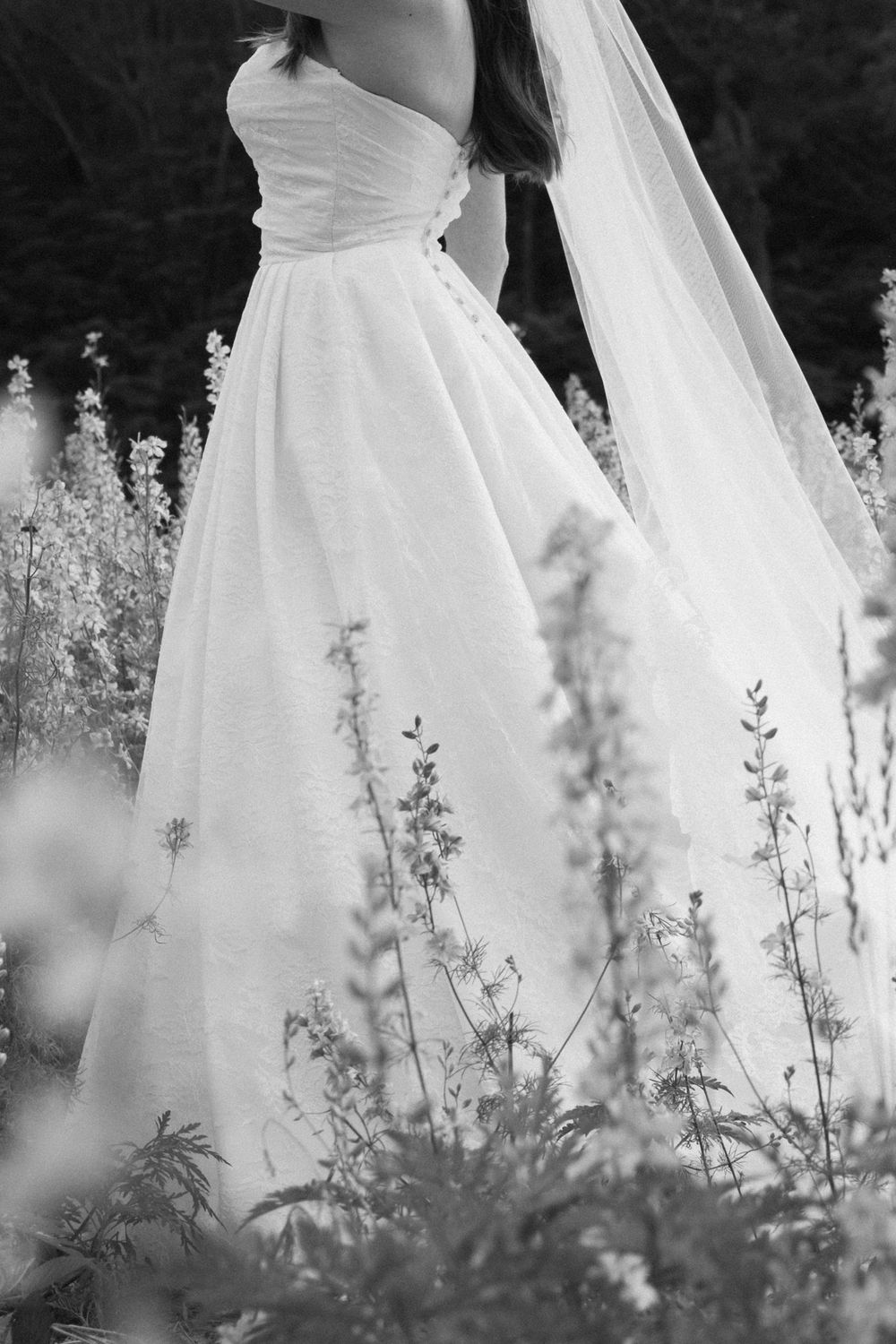A series of white wedding dresses photographed in black and white with delicate wildflowers in the foreground.