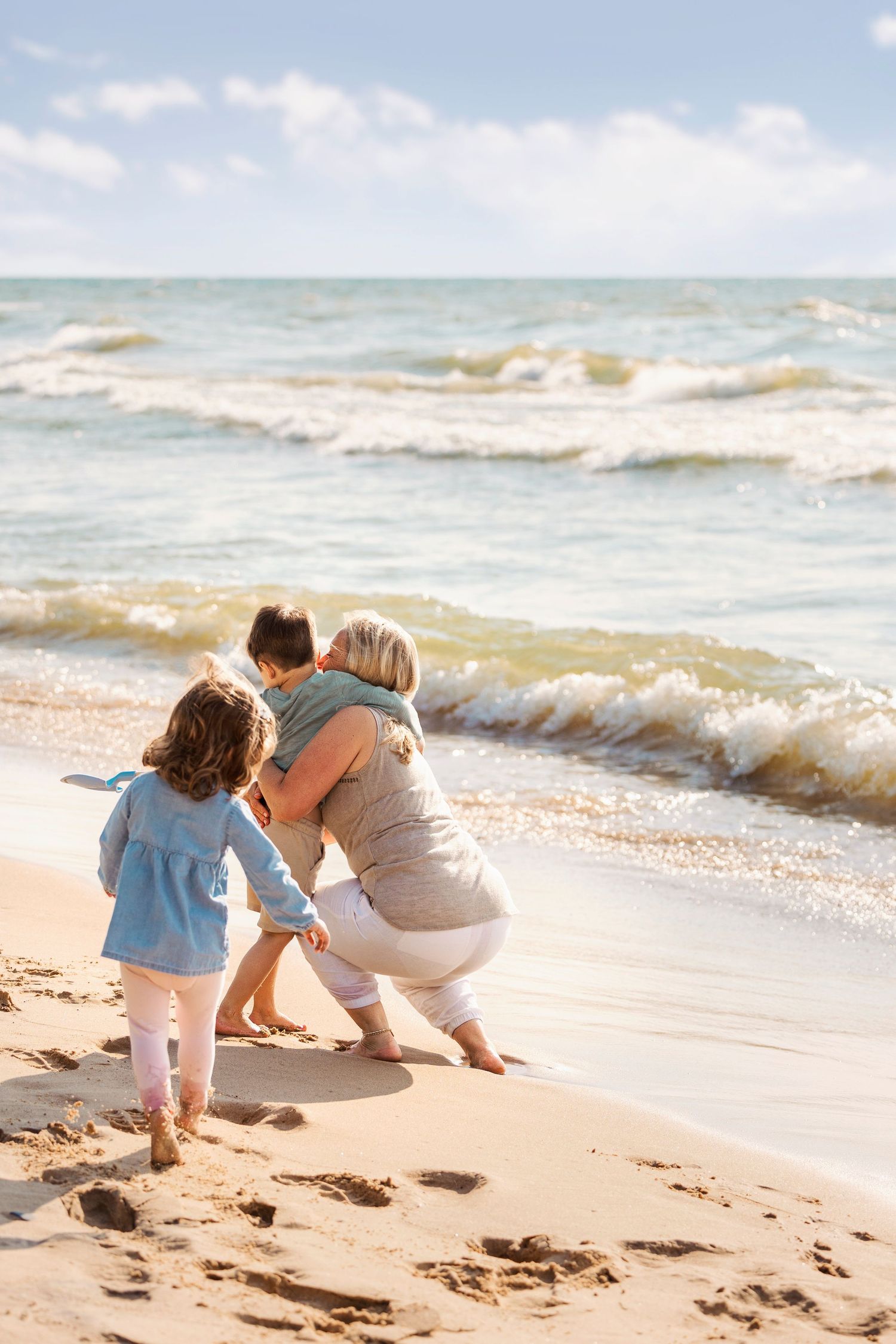 Sweet hug between mom and son near the waterline, feet in the sand and smiles all around.