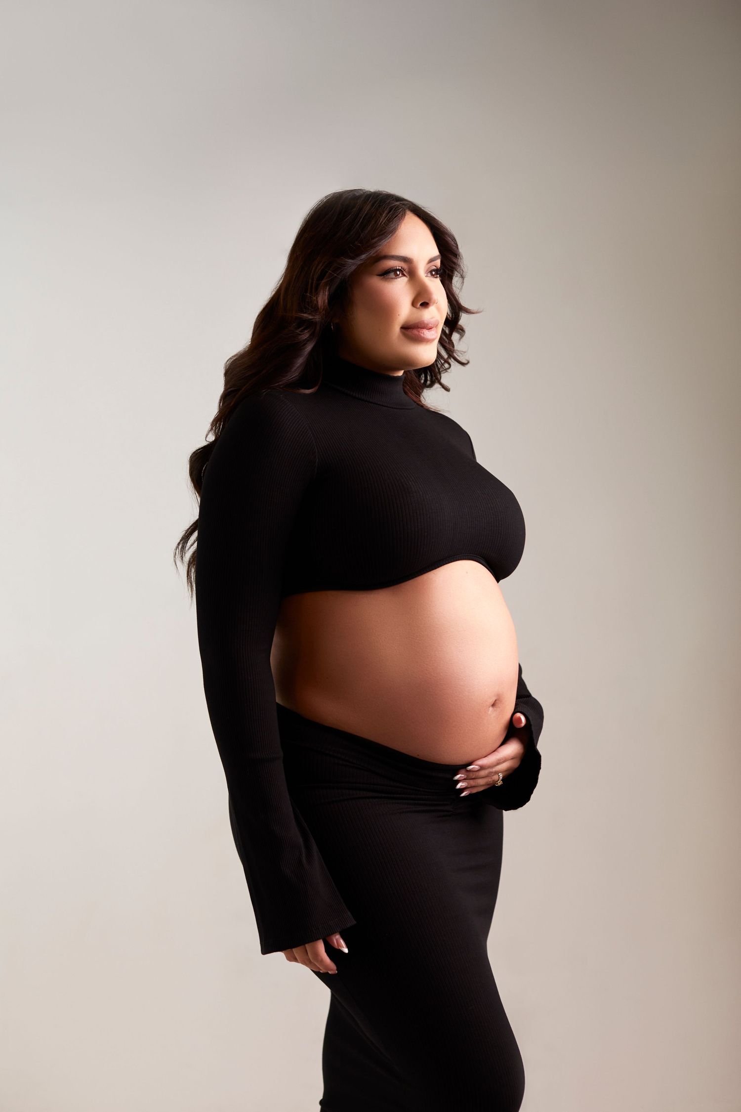 Artistic maternity photos showing woman in black dress against neutral background.