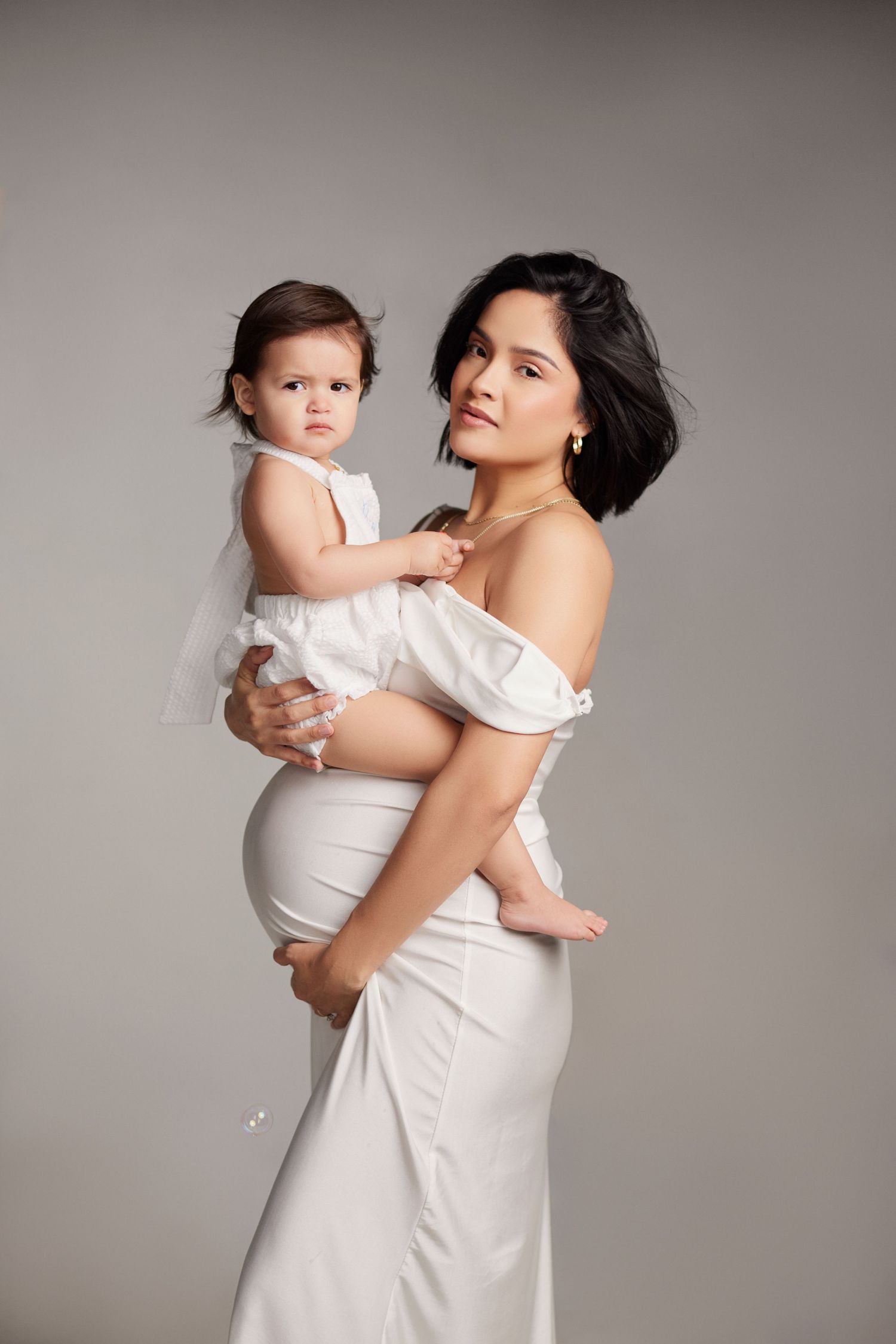 Mother and baby in white dresses pose together for studio portraits.