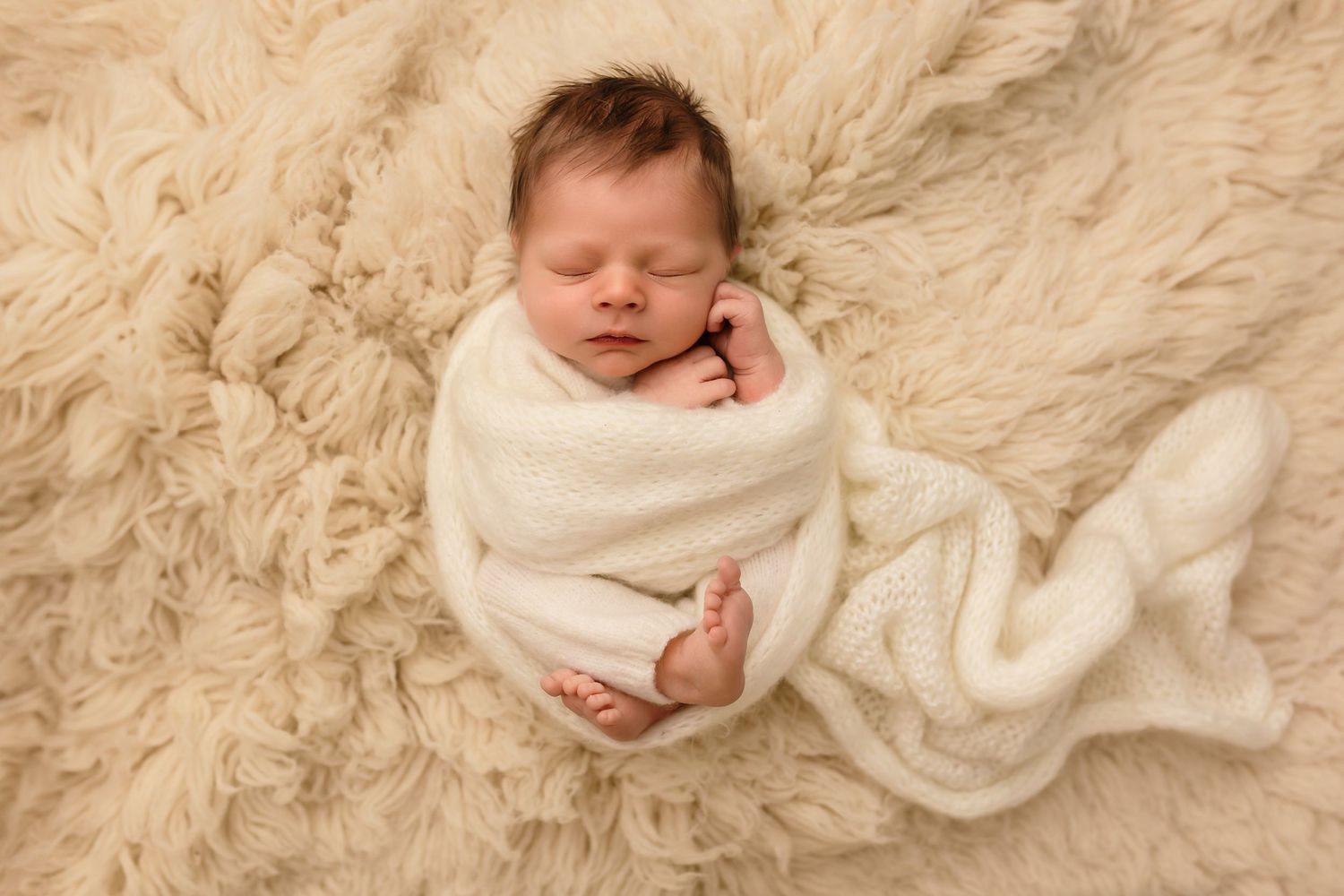 Charlottesville photographer, family, baby, and maternity; newborn boy wrapped in white knits sleeps against a warm cream wool rug.
