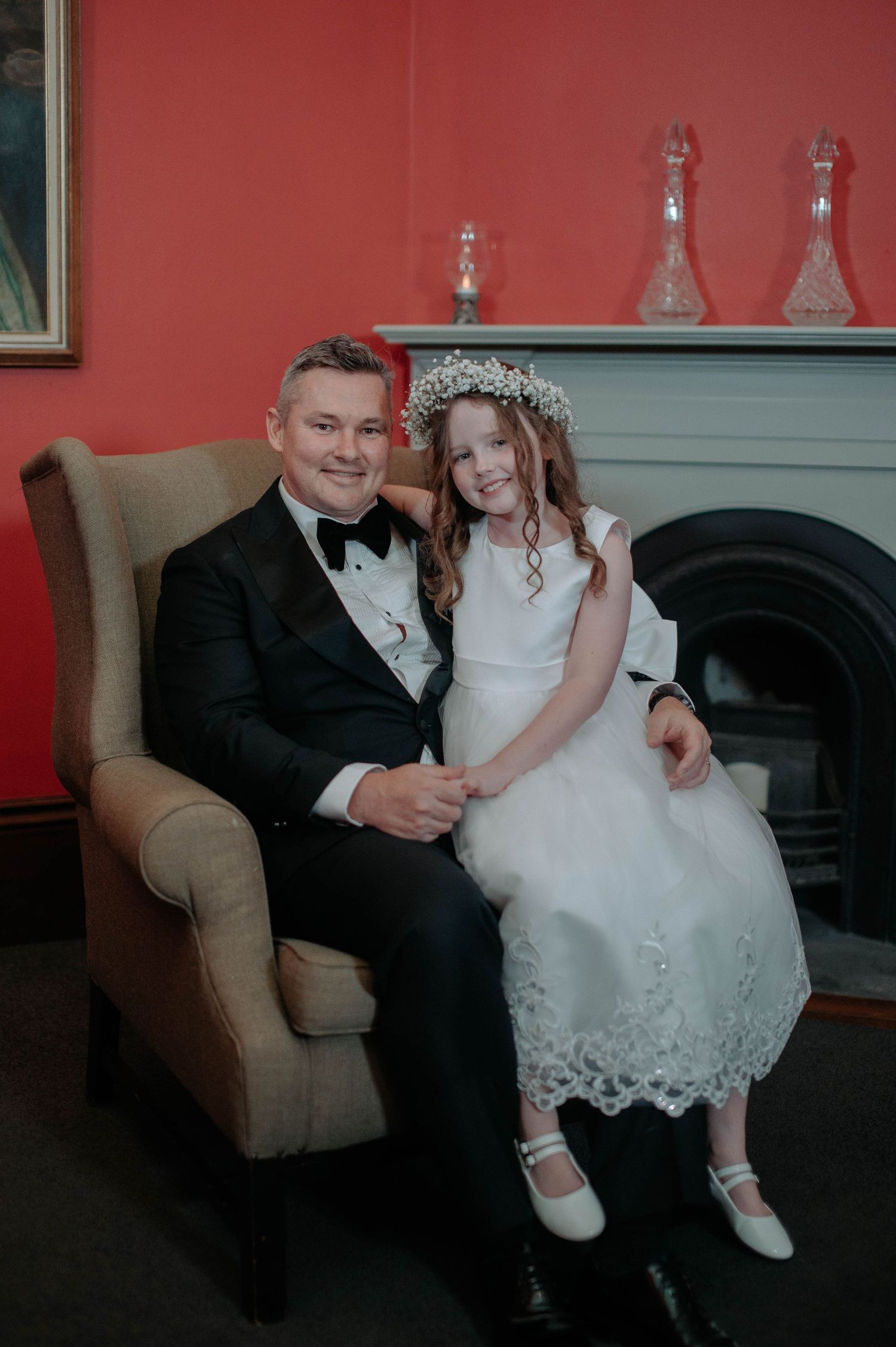 A formal wedding moment captured in front of a fireplace with ornate decor and red walls.