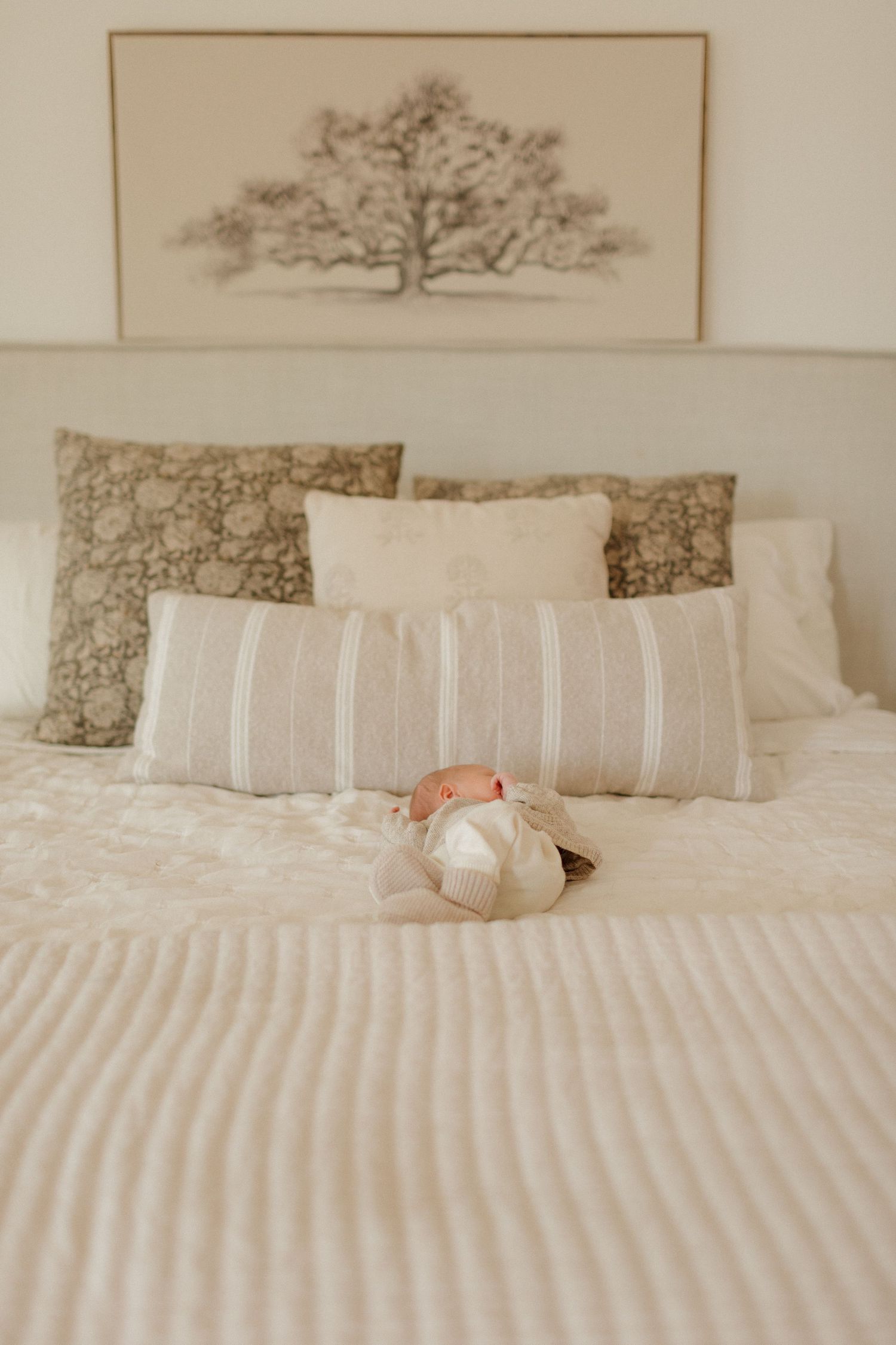 A white bed with decorative pillows in neutral colors and a striped pattern arranged neatly against a light wall.