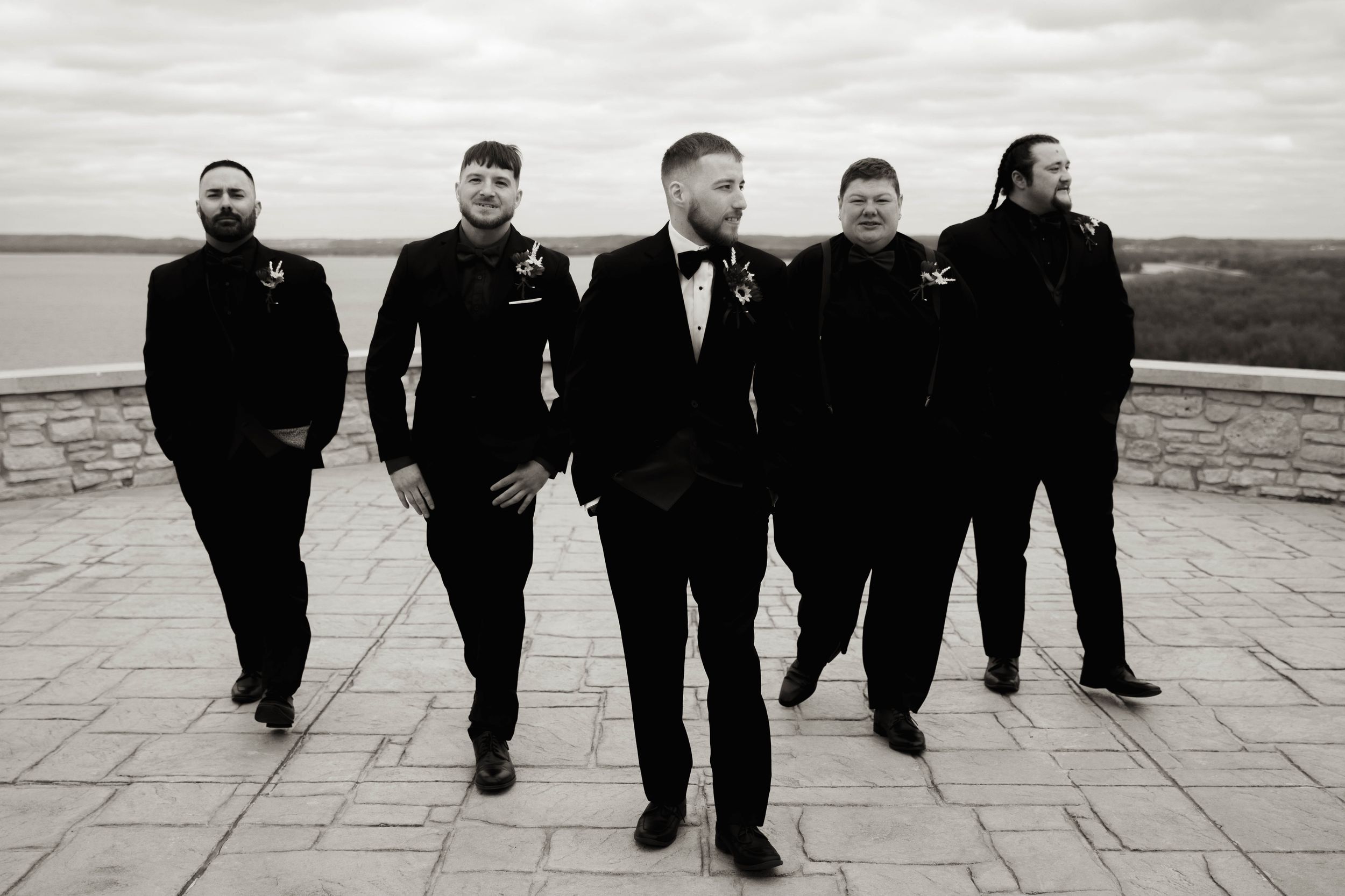 Groomsmen in black suits walking in a creative line formation on a stone patio.