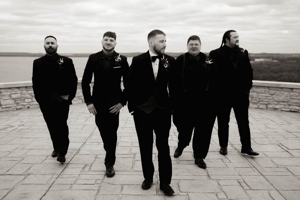Groomsmen in black suits walking in a creative line formation on a stone patio.